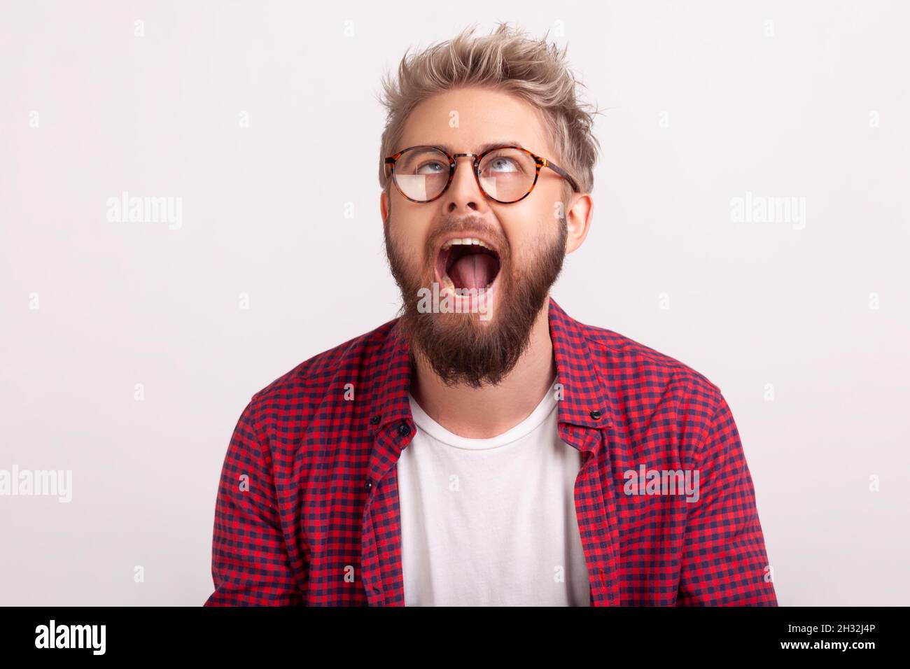 Porträt eines dummen bärtigen Mannes in einer Brille, die Augen kreuzt und mit geöffnetem Mund herumtollt, komische Darbietung. Innenaufnahme des Studios isoliert auf grauem Hintergrund Stockfoto