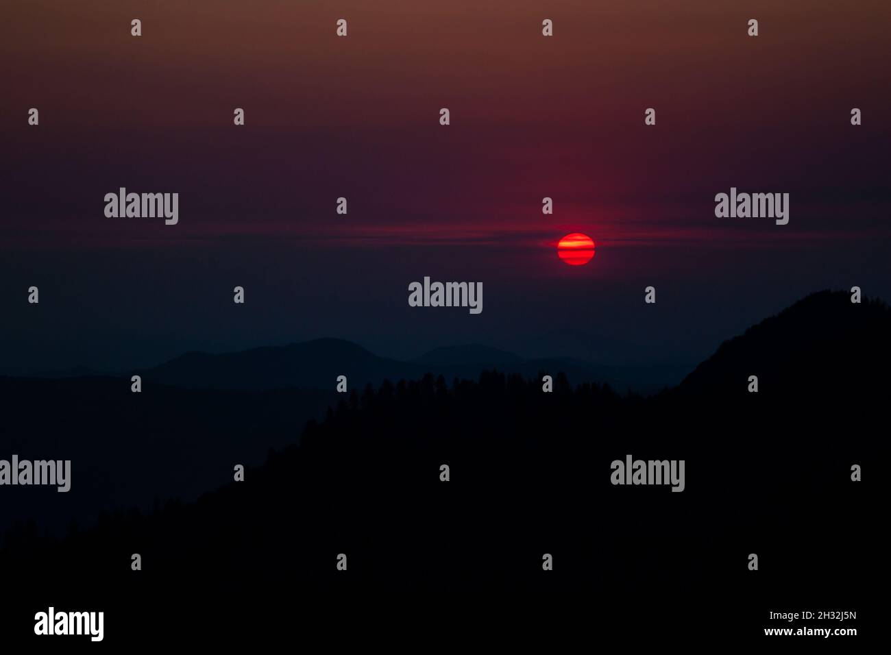 Landschaftlich schöner Sonnenuntergang über den Bergen, die von Wald überwuchert sind, schwarze Silhouette des Berges, rote Sonne, dunkler Himmel, Sonne im Moro Rock Sequoia NP teilweise verdunkelt Stockfoto