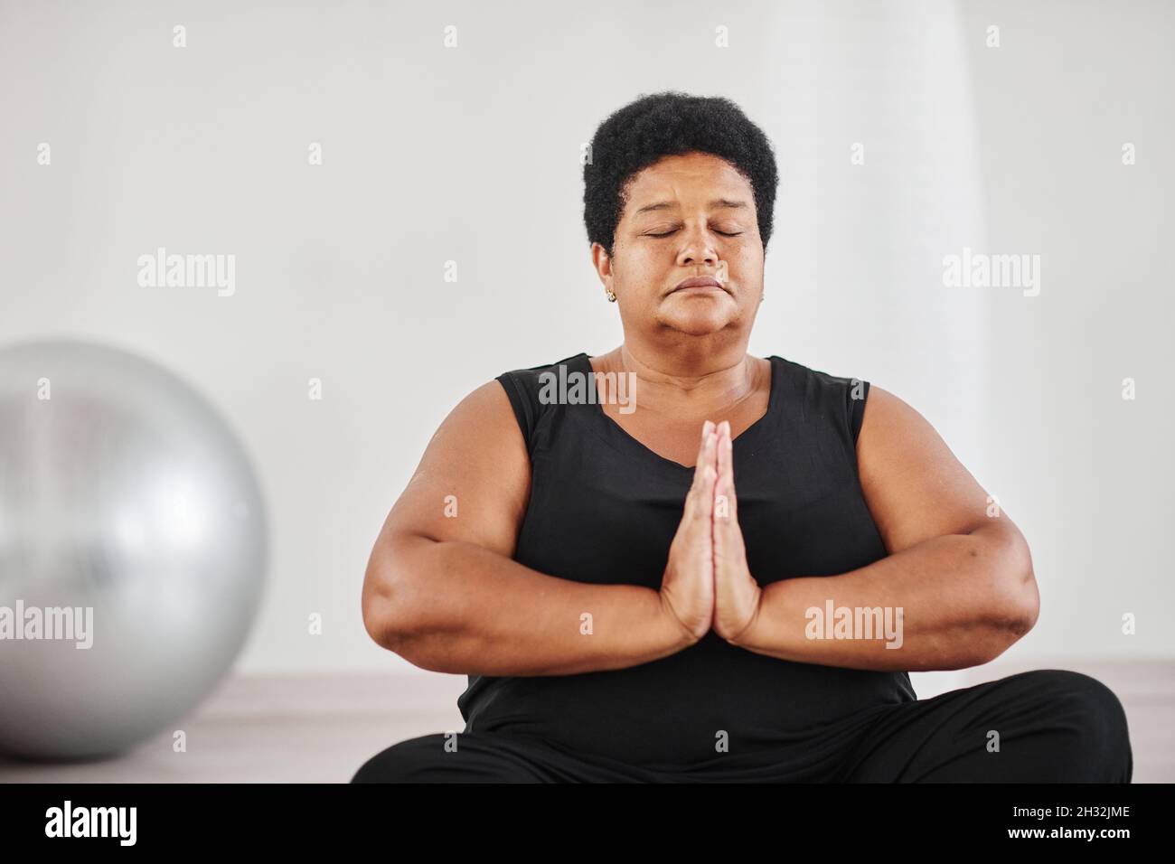 Porträt einer reifen afrikanischen, prallen Frau, die mit geschlossenen Augen in Lotusposition sitzt und während des Yoga meditiert Stockfoto
