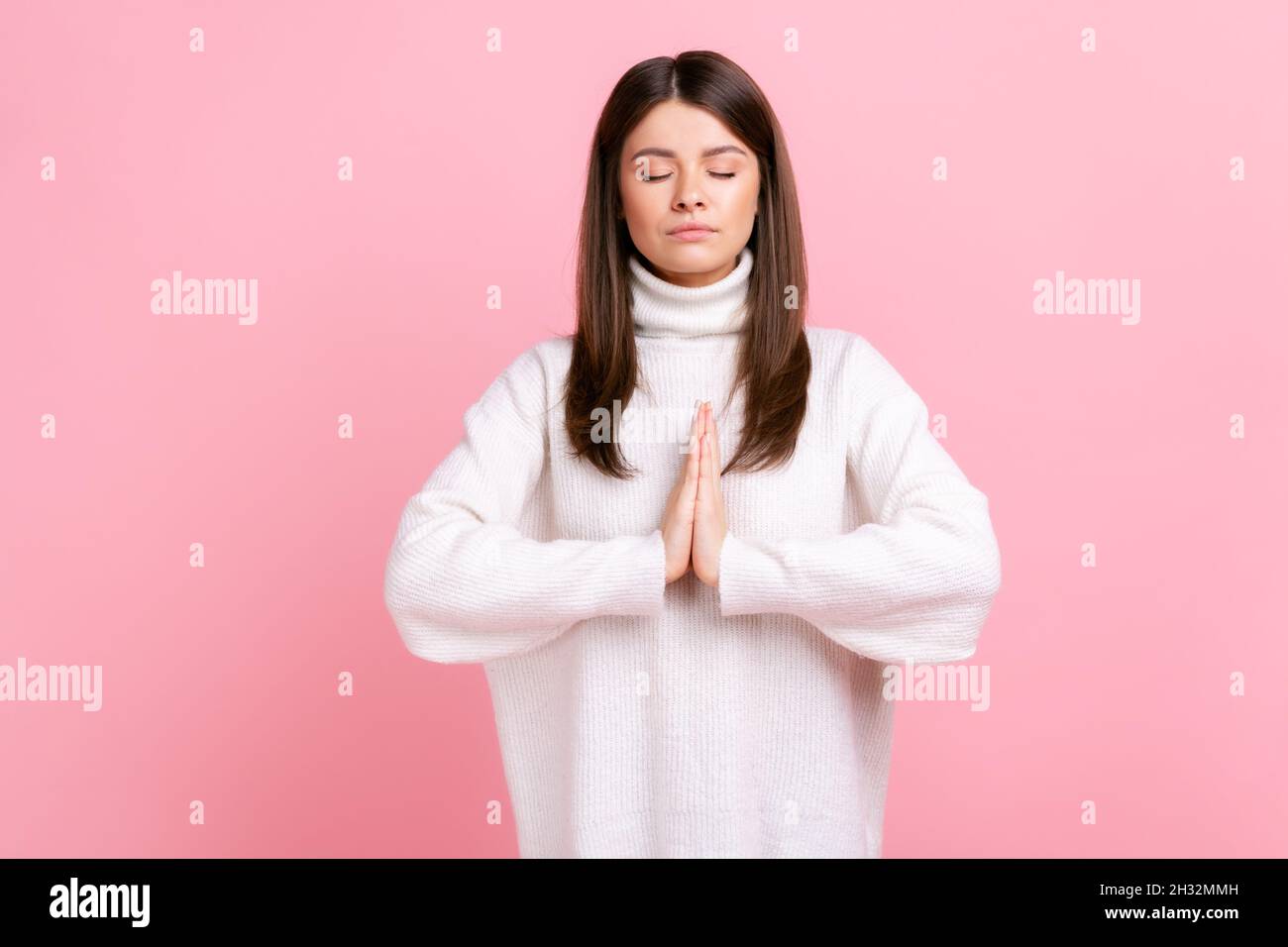 Ruhige, entspannte weibliche Stehen mit geschlossenen Augen, Atmung, Yoga-Training, Harmonie fühlen, tragen weißen Pullover im lässigen Stil. Innenaufnahme des Studios isoliert auf rosa Hintergrund. Stockfoto