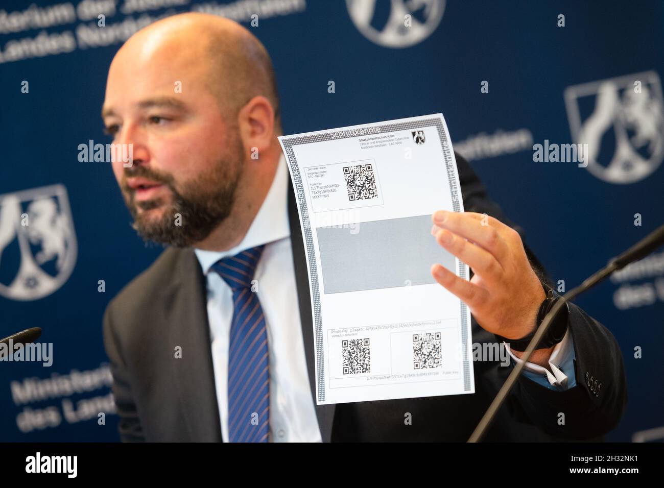Köln, Deutschland. Oktober 2021. Andreas Brück, Staatsanwalt am ZAC NRW,  zeigt während einer Pressekonferenz eine Papierbörse für Bitcoin. Die  Nordrhein-westfälische Justiz hat zum ersten Mal mit der Versteigerung von  beschlagnahmten Bitcoin begonnen.