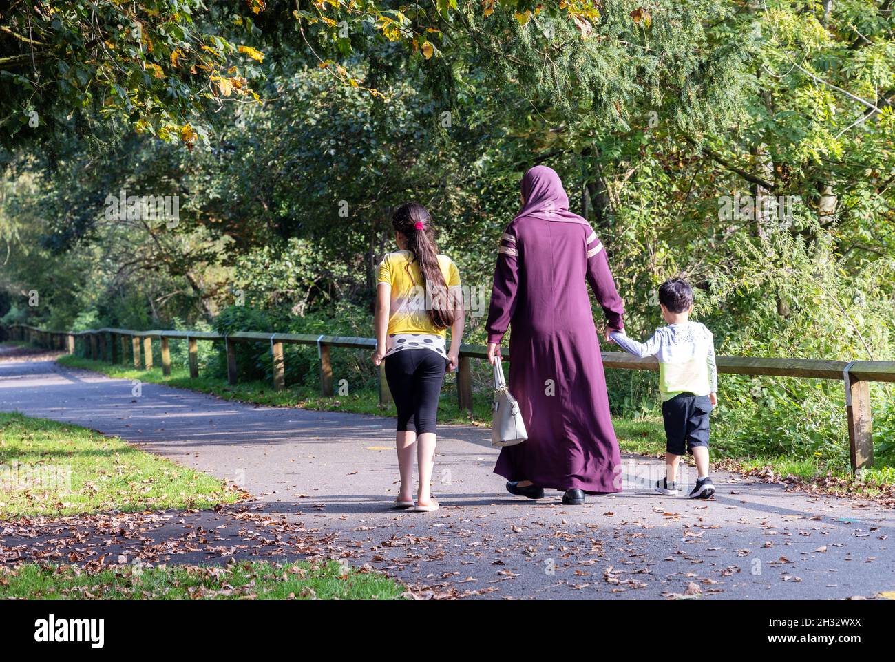 Arabische Familie Großbritannien; eine muslimische Mutter und ihre zwei Kinder, die im Park spazieren, von hinten gesehen, Salisbury Wiltshire Großbritannien Stockfoto