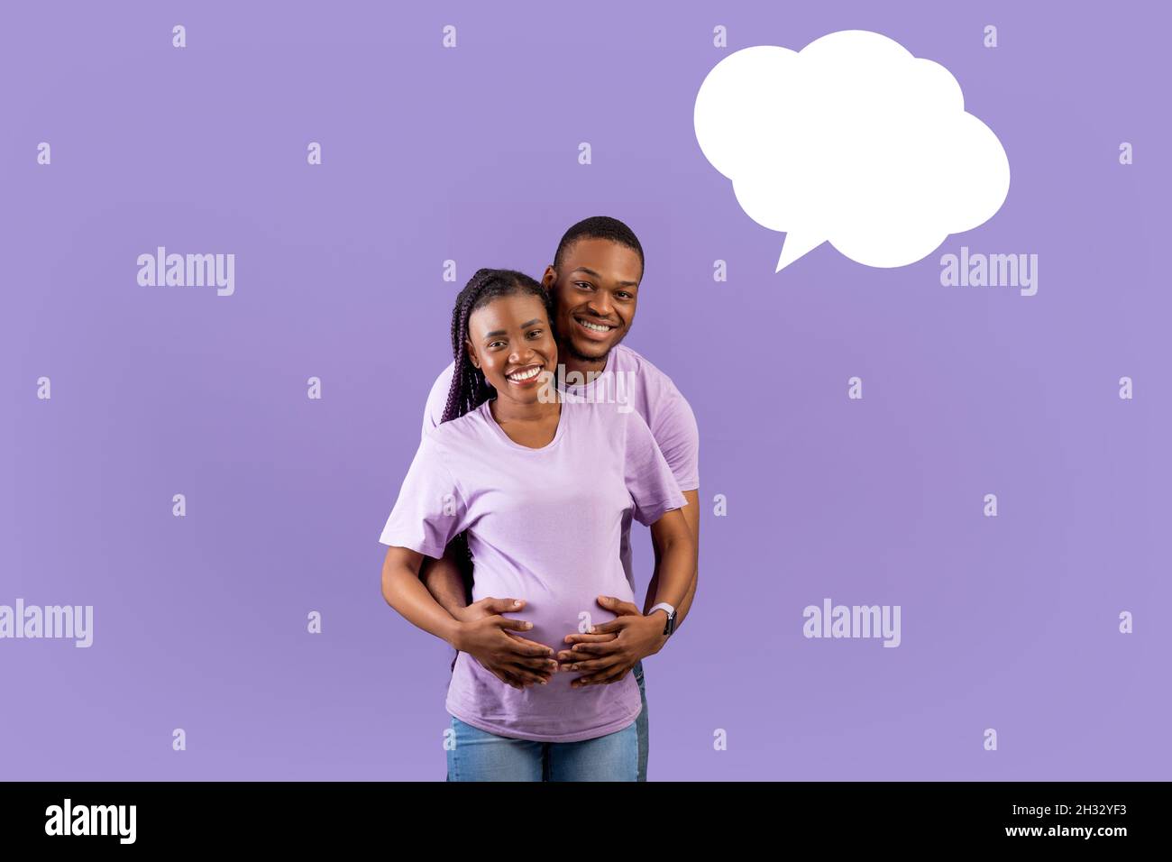 Porträt eines lächelnden schwarzen Mannes, der die Schwangeren von hinten umarmt, ein fröhliches Paar, das über den violetten Hintergrund des Studios steht und an das Baby-na denkt Stockfoto