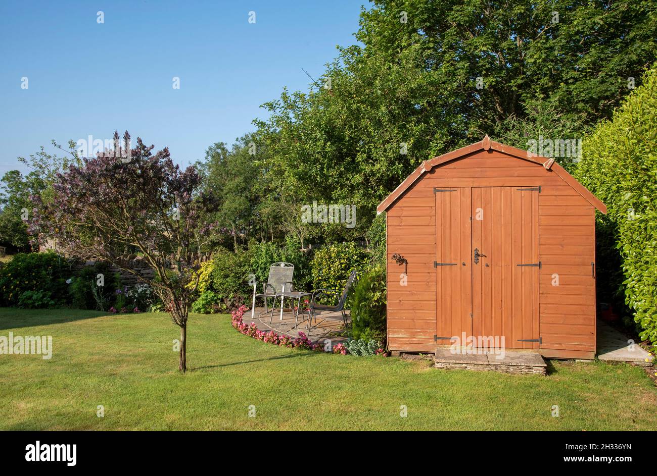 Devon, England, Großbritannien. 2021. Ein holländischer Gartenschuppen im Scheunenstil mit Doppeltüren, die mit Terrasse, Tischen und Stühlen in einem englischen Landgarten stehen. Stockfoto