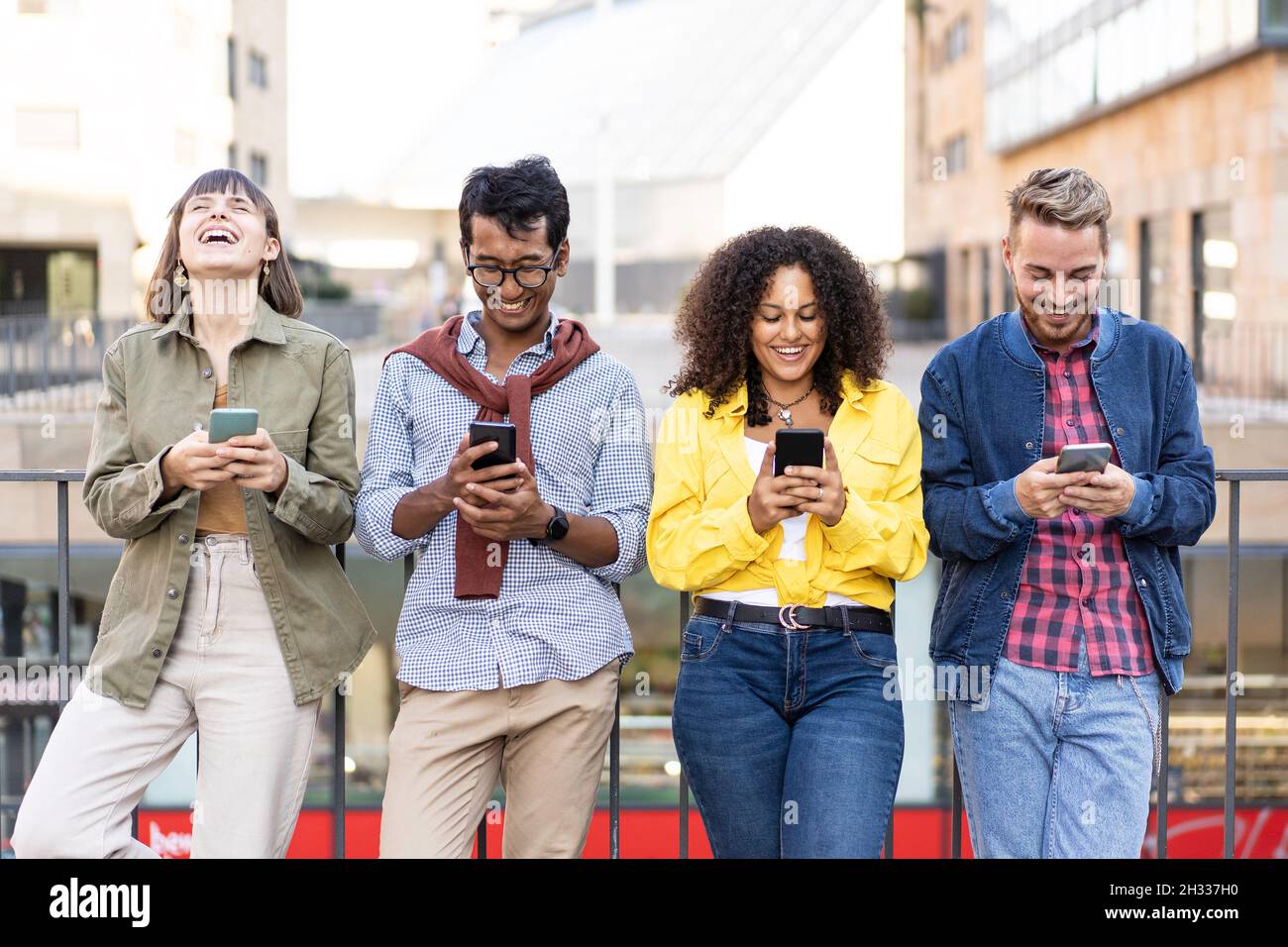 Multirassische Freunde, die im Universitätsviertel der Stadt mit dem Smartphone lachen - Junge Menschen, die von Mobiltelefonen süchtig sind - Technologie-Conce Stockfoto