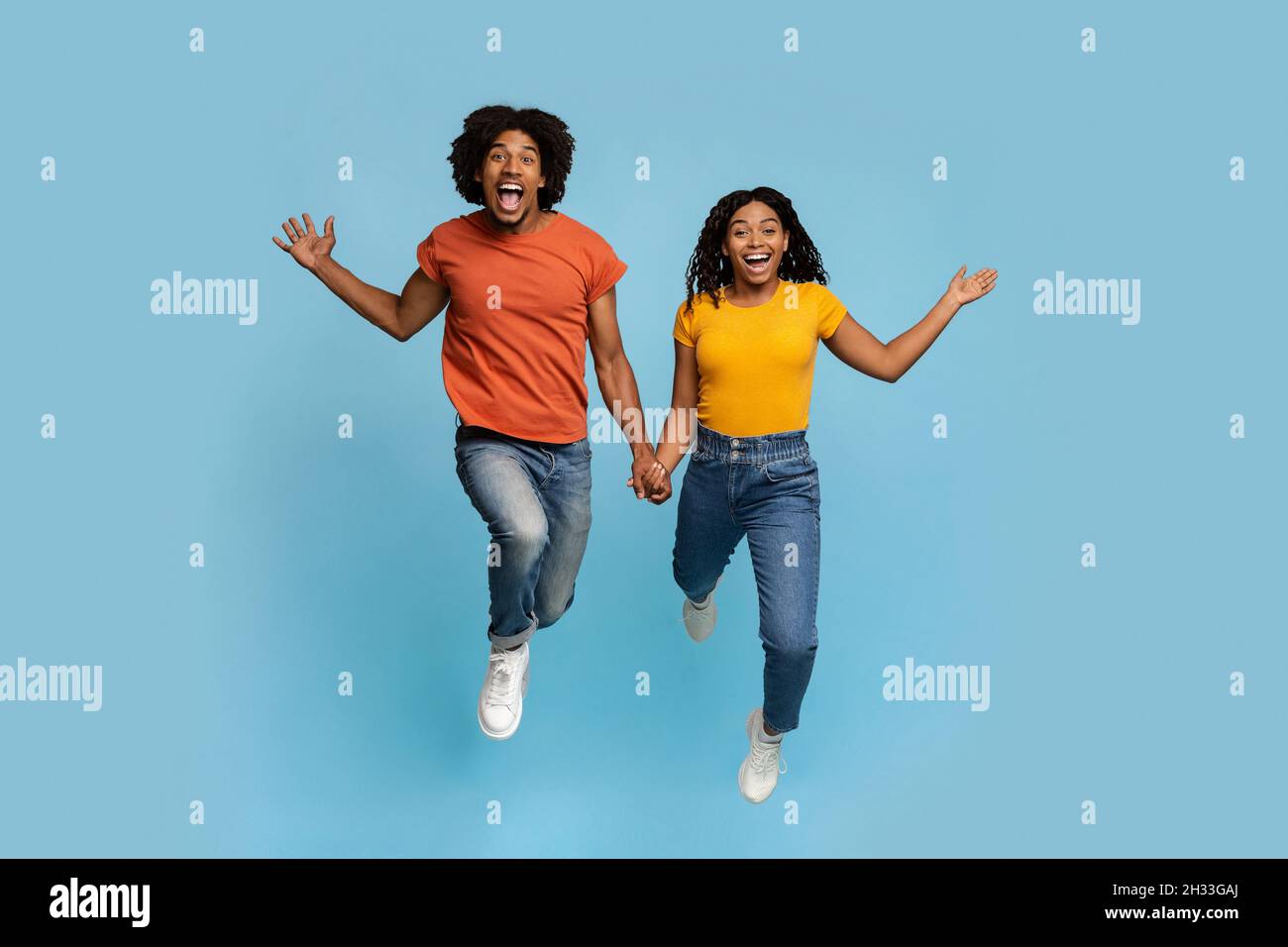 Begeisterte afroamerikanische Liebhaber halten sich die Hände, während sie über den blauen Studiohintergrund laufen, glücklicher schwarzer Mann und Frau genießen jeden einzelnen Moment zusammen Stockfoto