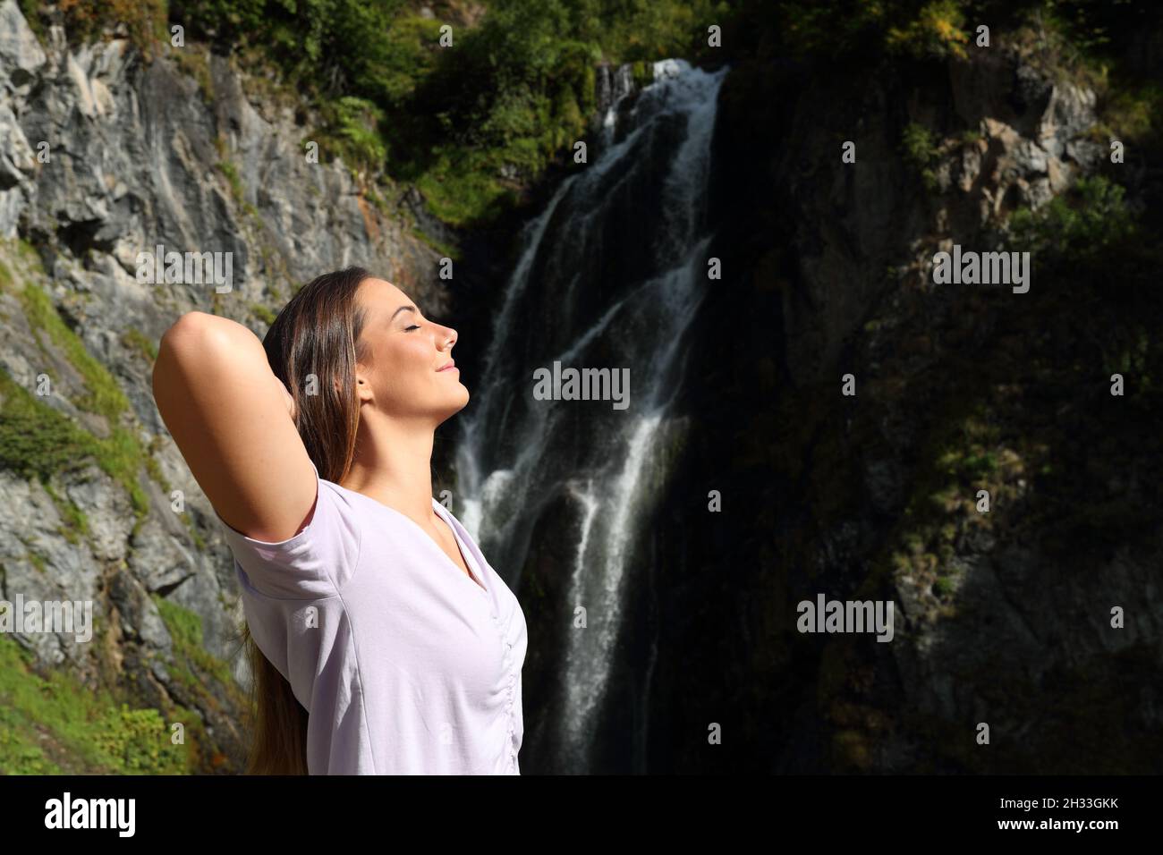 Seitenansicht Porträt einer glücklichen, entspannten Frau, die frische Luft atmet und in einem Wasserfall ruht Stockfoto