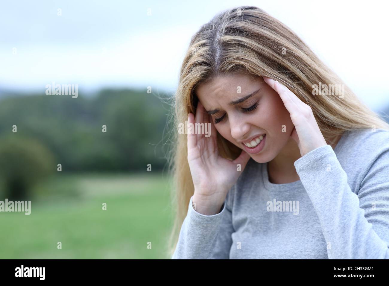 Gestresster Teenager, der sich auf einem Feld über einen Migräneanfall beschwert Stockfoto