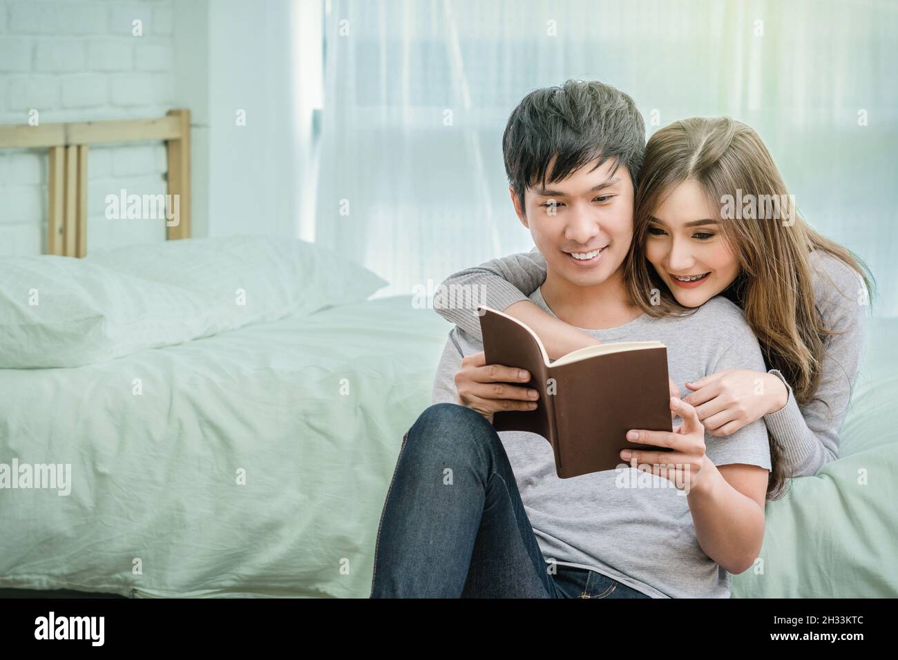 Glücklicher asiatischer Liebhaber oder Paar beim Lesen des Notebooks auf dem Bett im Schlafzimmer zu Hause, Paar und Lifestyle-Konzept, Stockfoto