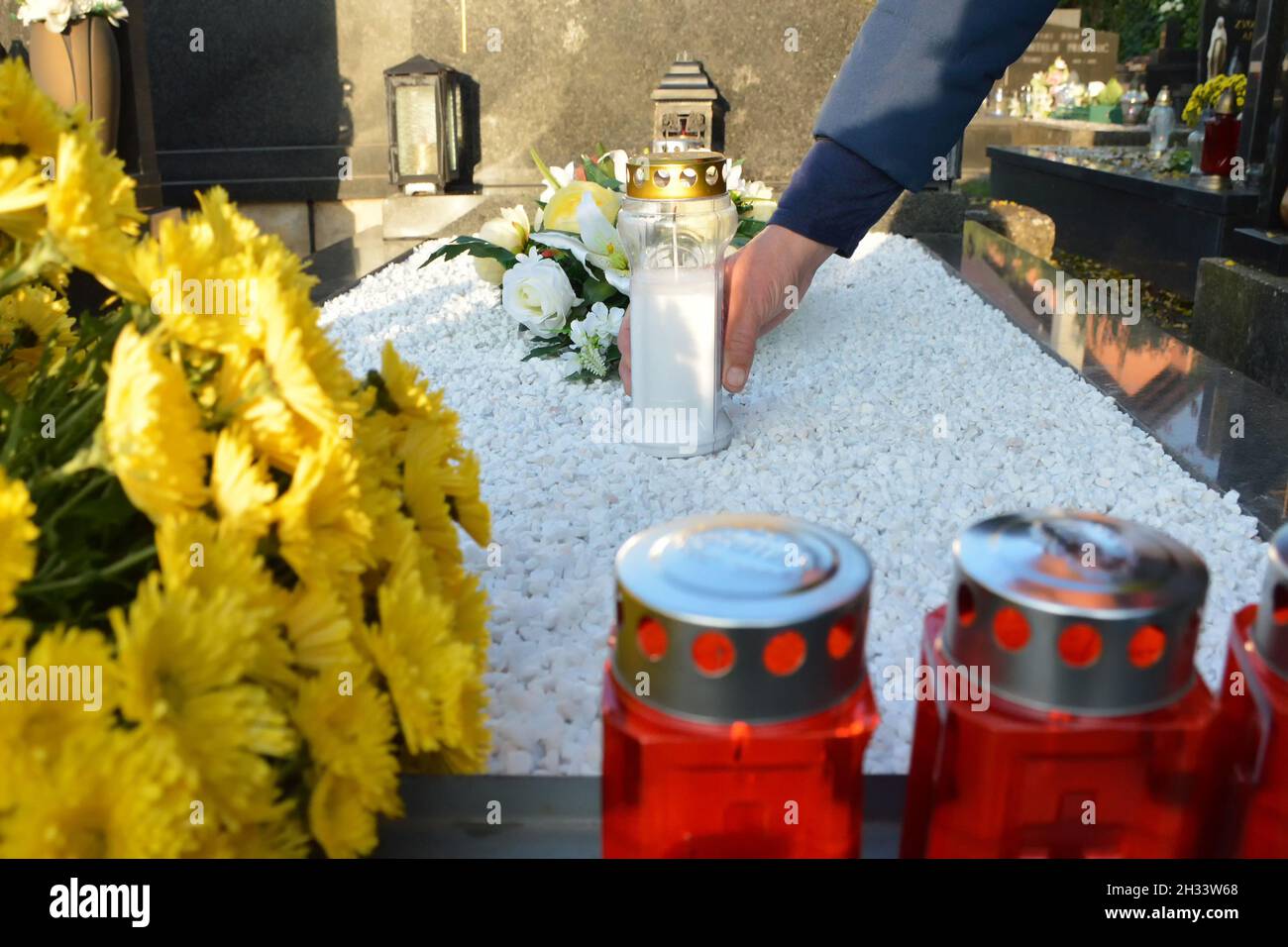 Mann, der eine weiße Votivkerze auf das Grab legt Stockfoto