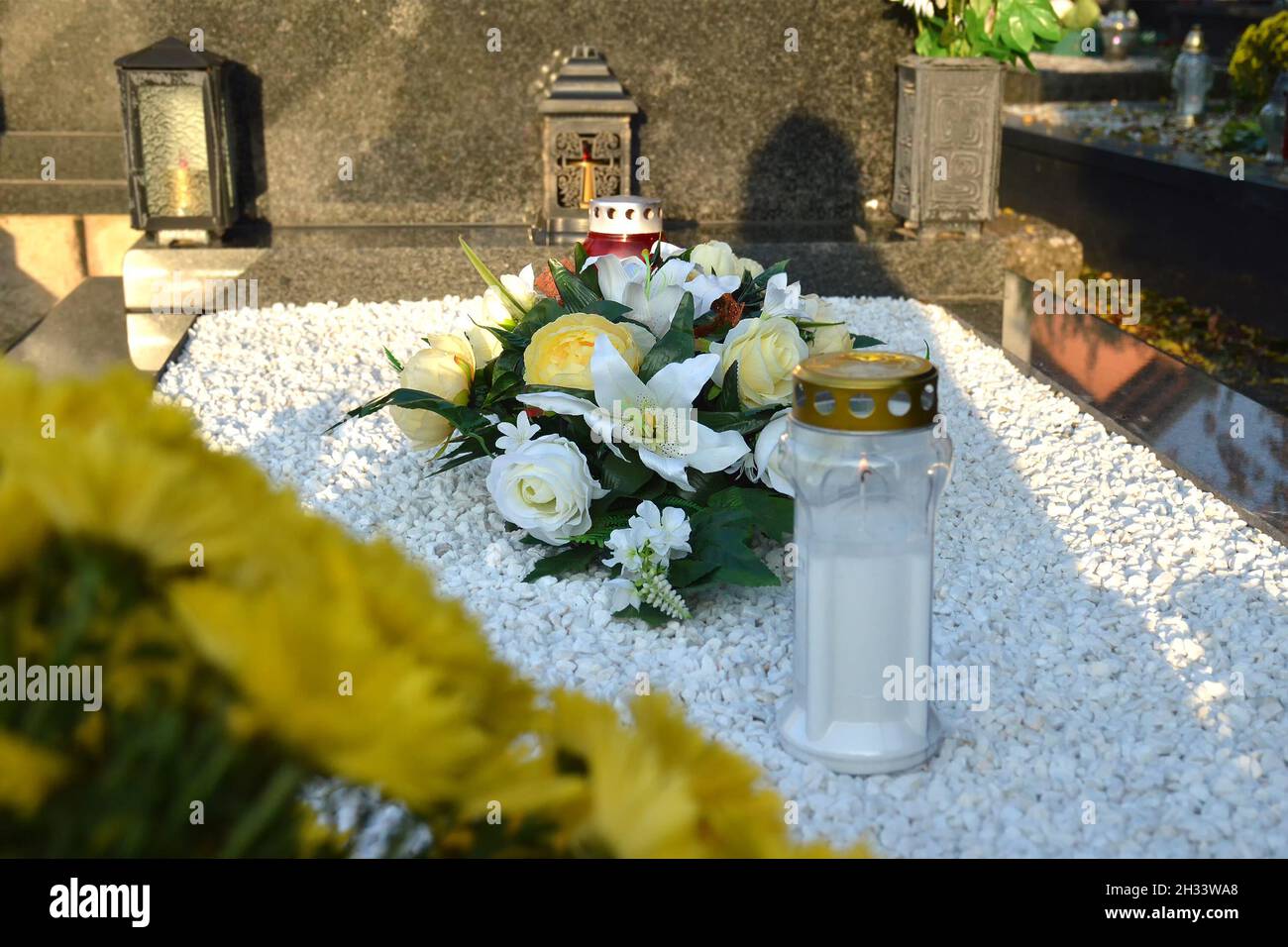 Blumen und weiße Votivkerze auf dem Grab Stockfoto