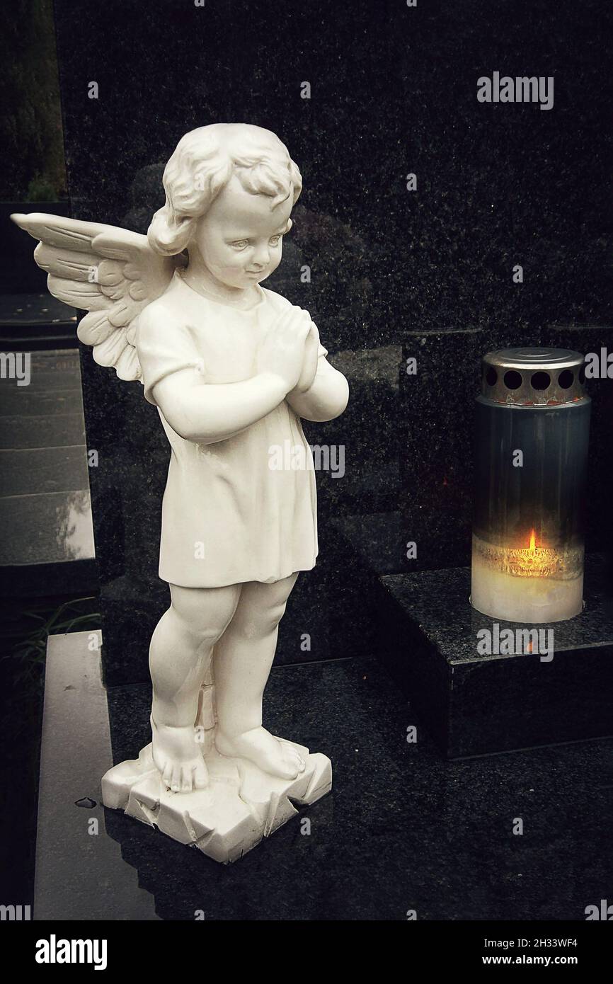 Schutzengel-Figur und brennende Kerze auf dem Grab Stockfoto
