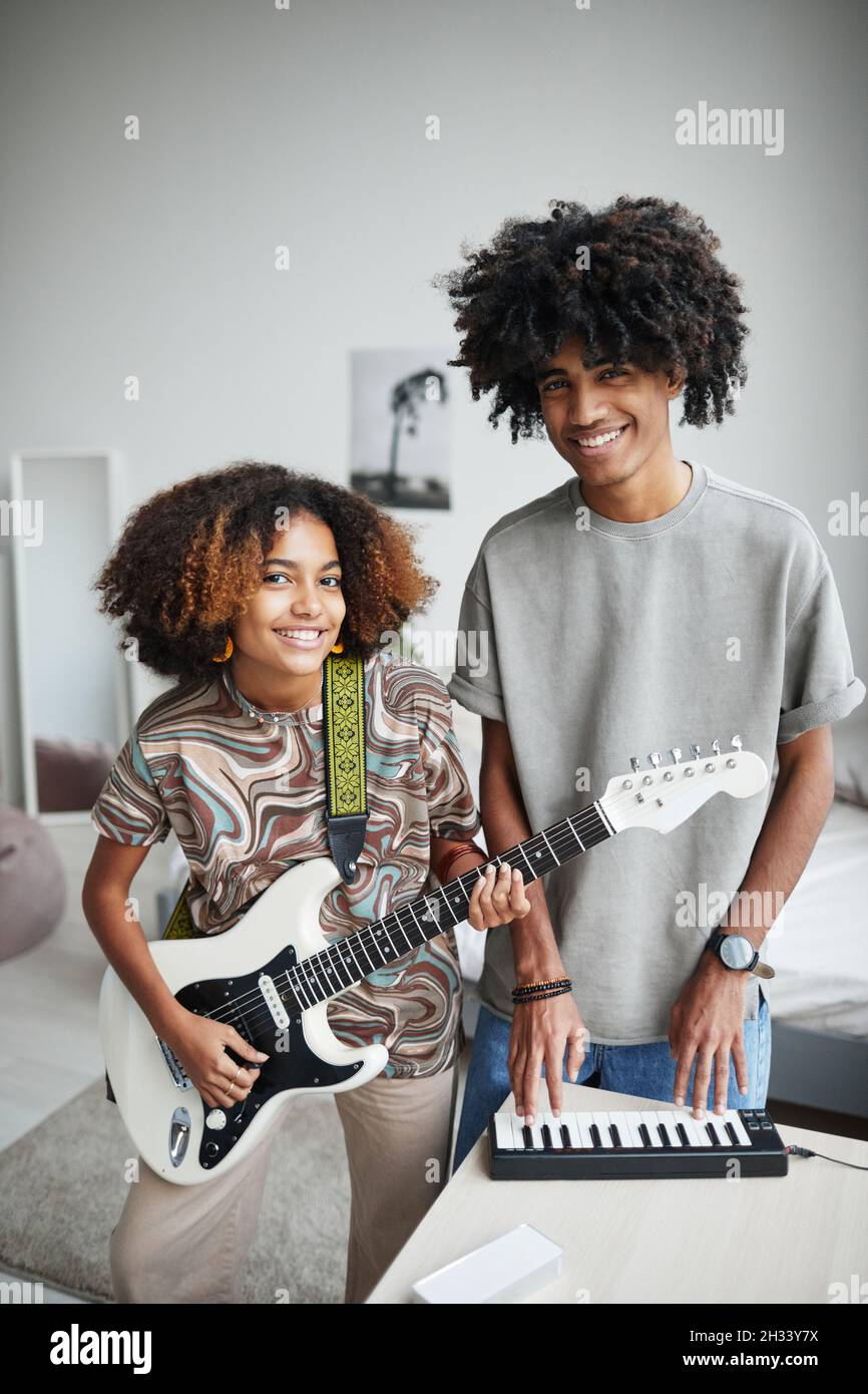 Vertikales Porträt zweier afroamerikanischer junger Menschen, die zu Hause Musik spielen und die Kamera, den Bruder und die Schwester anlächeln Stockfoto