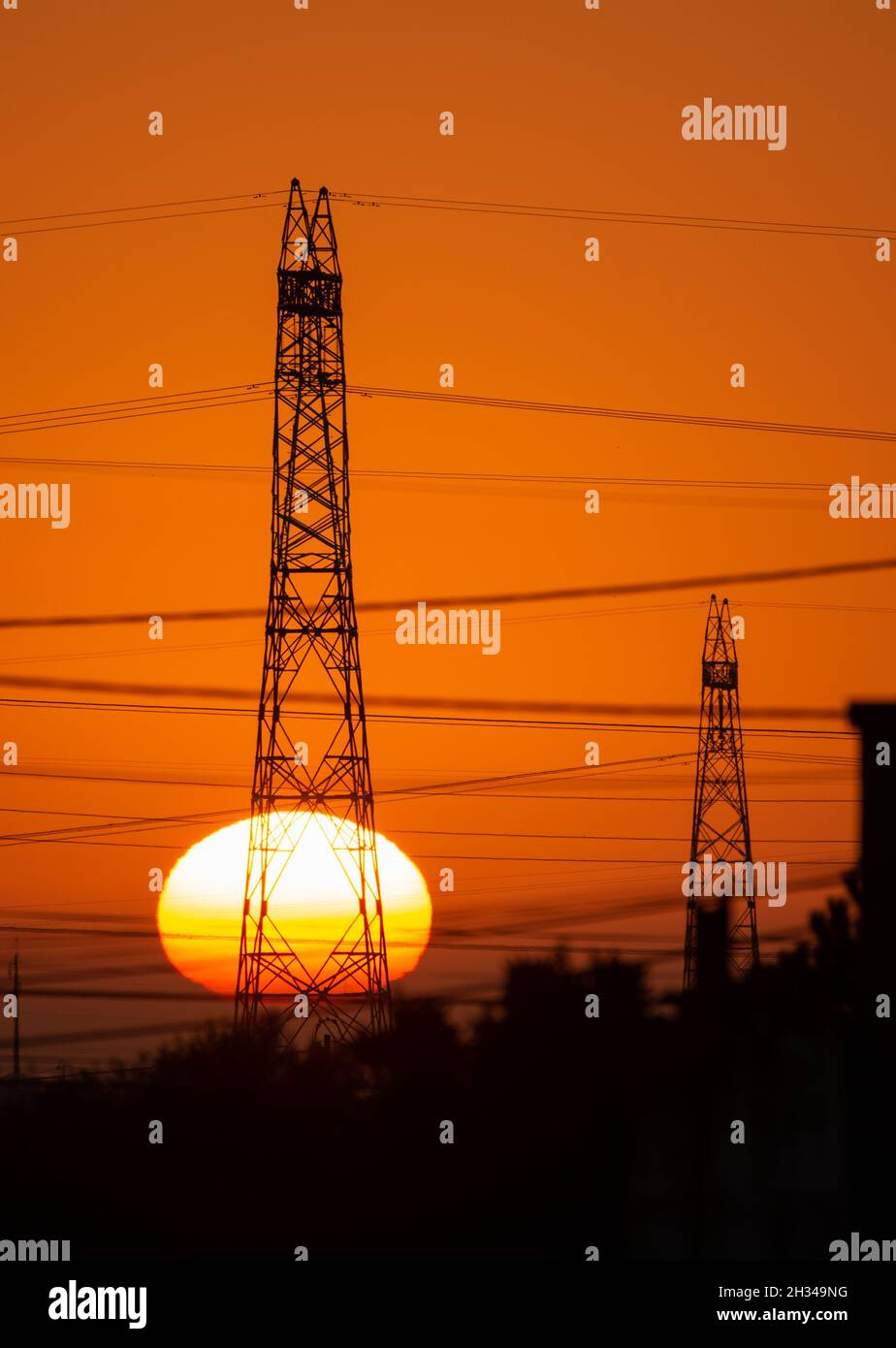 Strommasten und Stromleitungen bei Sonnenaufgang mit großer Sonne am Horizont. Portugal, Europa Stockfoto