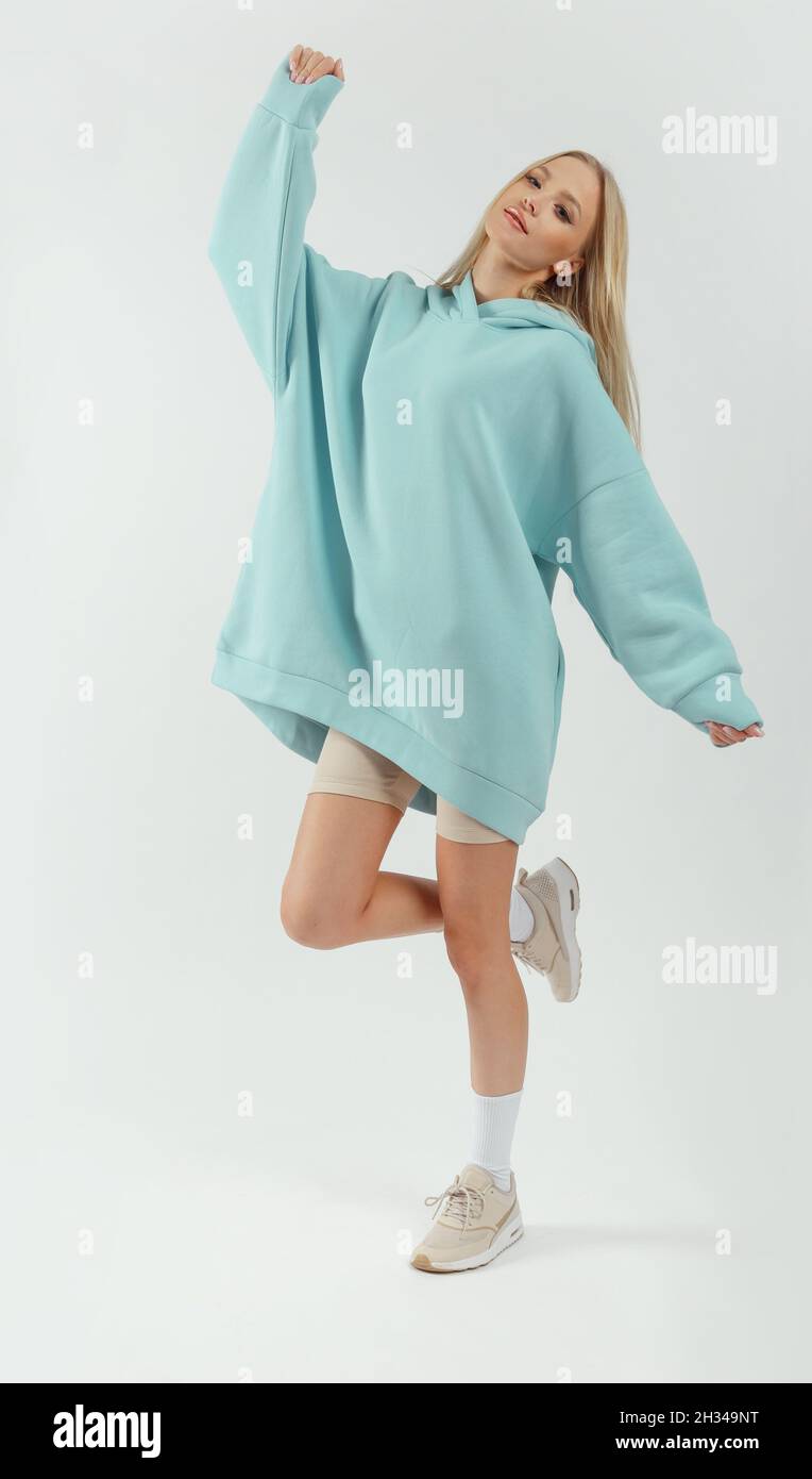 Junge hübsche Frau mit türkisfarbenem Hoodie und grauen Radhosen auf weißem Hintergrund. Lässiger Damen-Sportlook Stockfoto