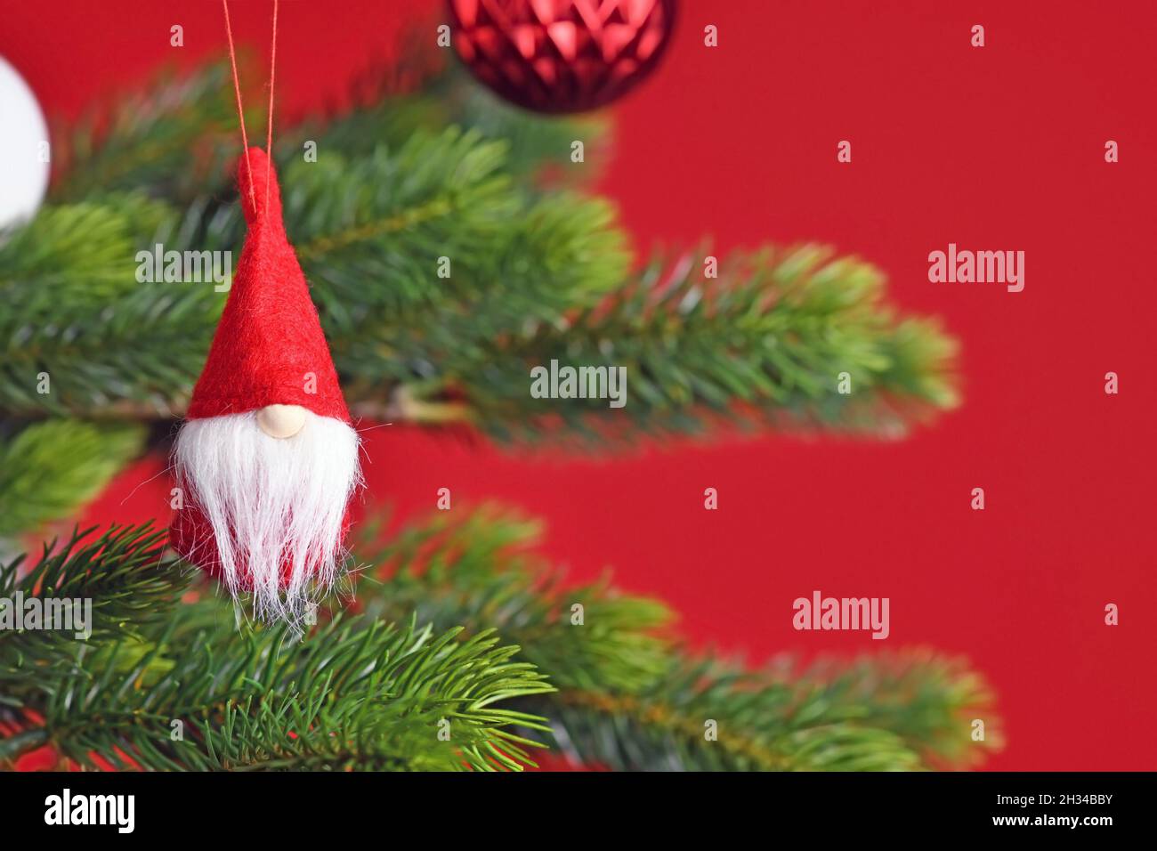Geschmückter Weihnachtsbaum mit niedlichem Weihnachtsgnome-Baumschmuck auf rotem Hintergrund Stockfoto