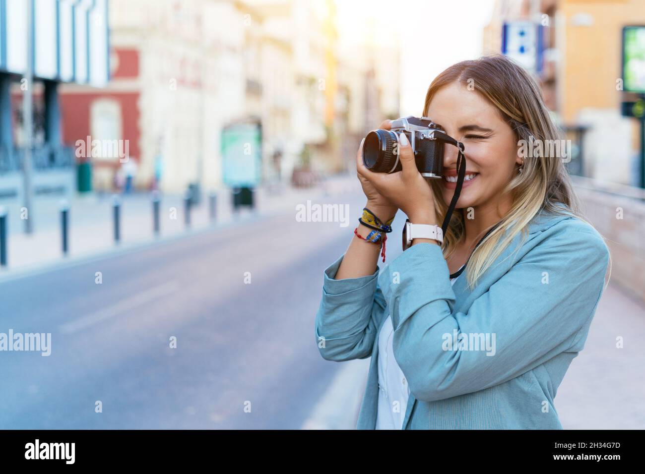 Lächelnde Frau, die in der Stadt mit der Kamera fotografiert Stockfoto