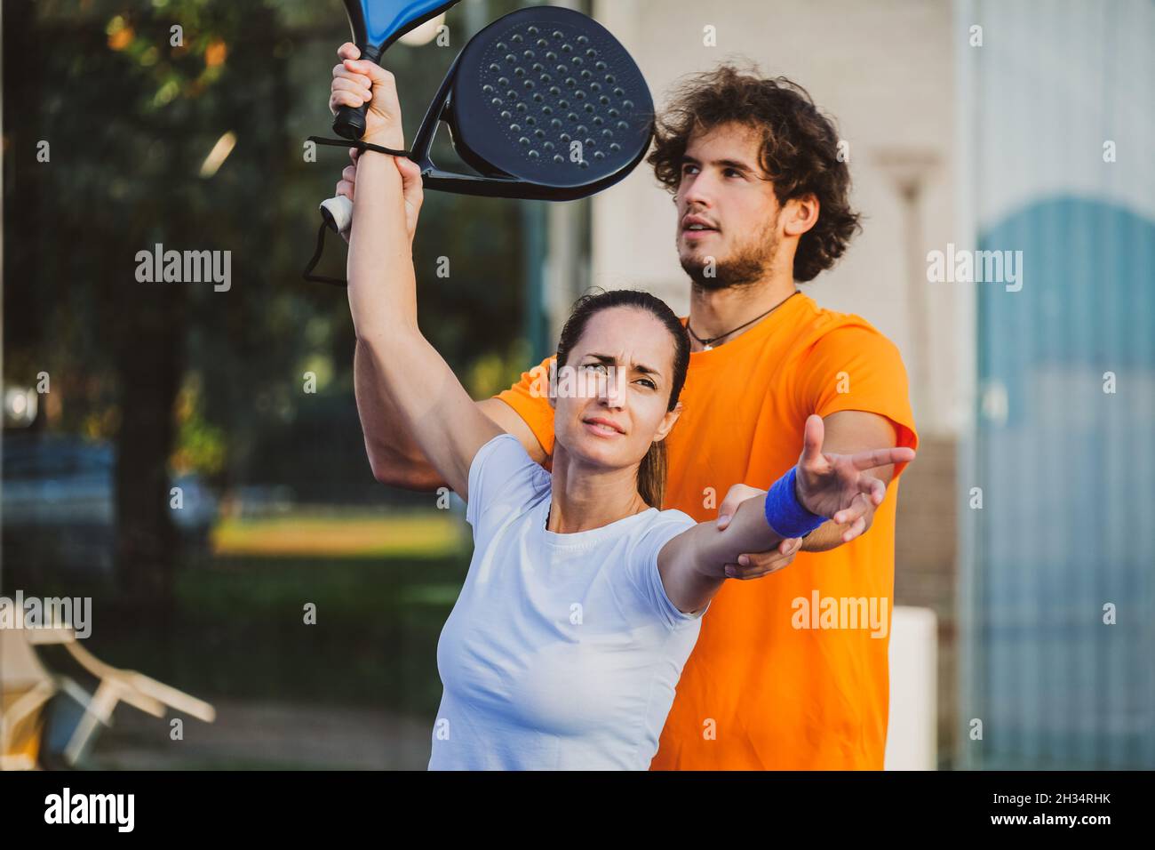 Der junge Lehrer überwacht den Padel-Unterricht für seine Schülerin - Coach lehrt Mädchen, wie man Padel auf dem Tennisplatz im Freien spielt Stockfoto