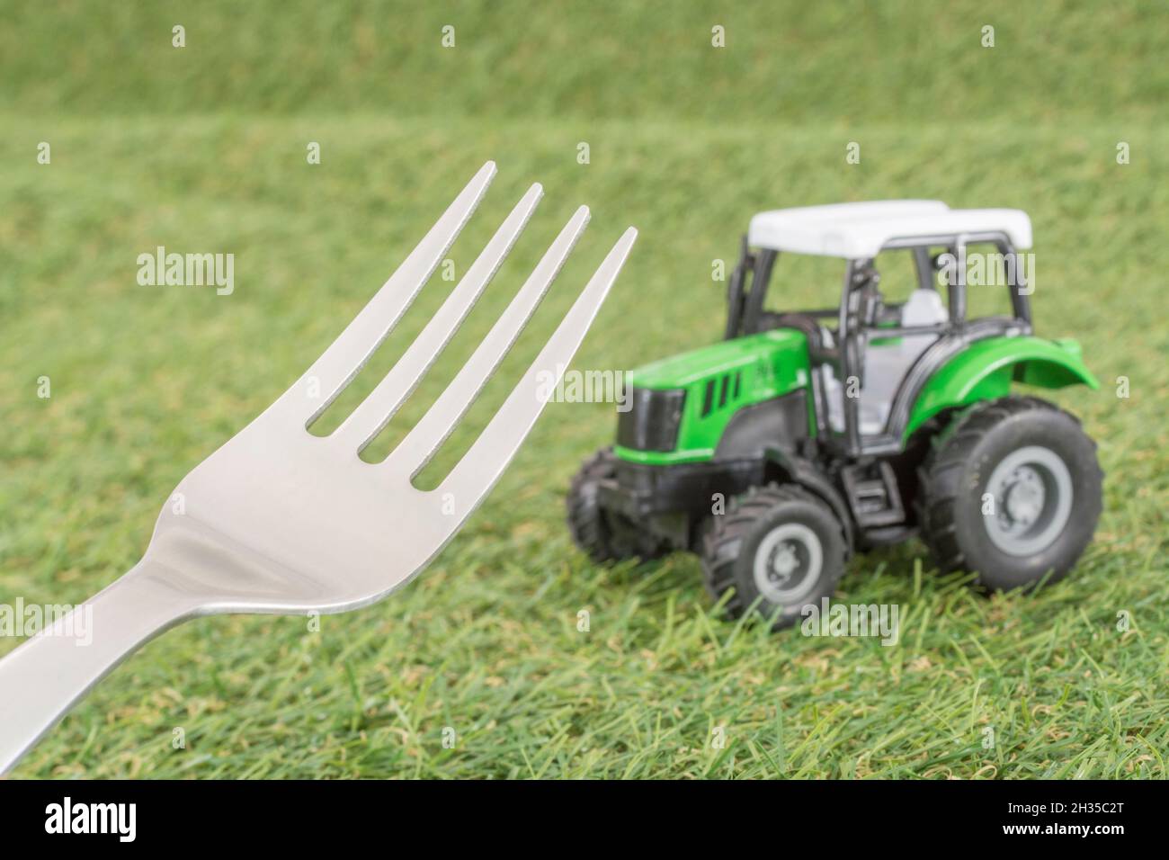 Kleiner Spielzeugschlepper auf faux/fake Gras mit Edelstahlgabelzinken. Für die britische Lebensmittelproduktion: Farm to Fork, Field to Fork / Field to Plate Idiome. Stockfoto
