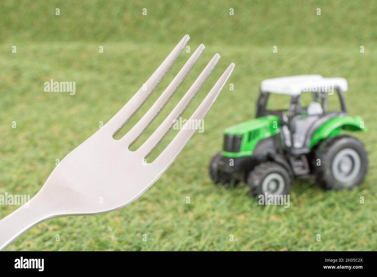 Kleiner Spielzeugschlepper auf faux/fake Gras mit Edelstahlgabelzinken. Für die britische Lebensmittelproduktion: Farm to Fork, Field to Fork / Field to Plate Idiome. Stockfoto