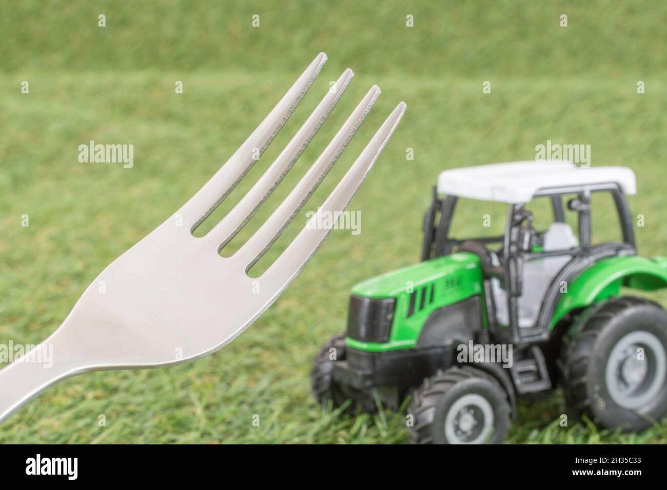 Kleiner Spielzeugschlepper auf faux/fake Gras mit Edelstahlgabelzinken. Für die britische Lebensmittelproduktion: Farm to Fork, Field to Fork / Field to Plate Idiome. Stockfoto