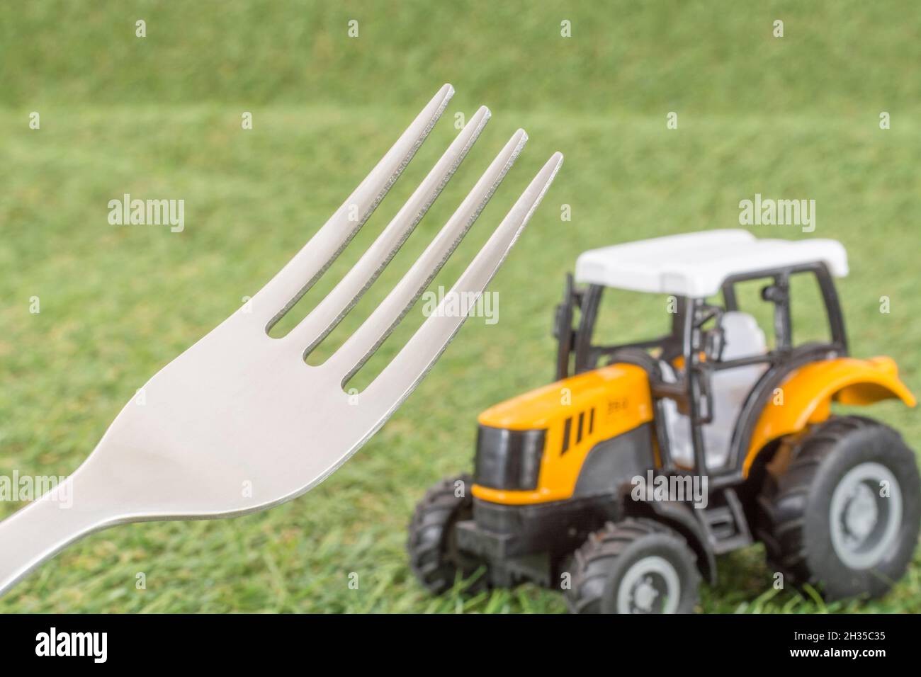 Kleiner Spielzeugschlepper auf faux/fake Gras mit Edelstahlgabelzinken. Für die britische Lebensmittelproduktion: Farm to Fork, Field to Fork / Field to Plate Idiome. Stockfoto