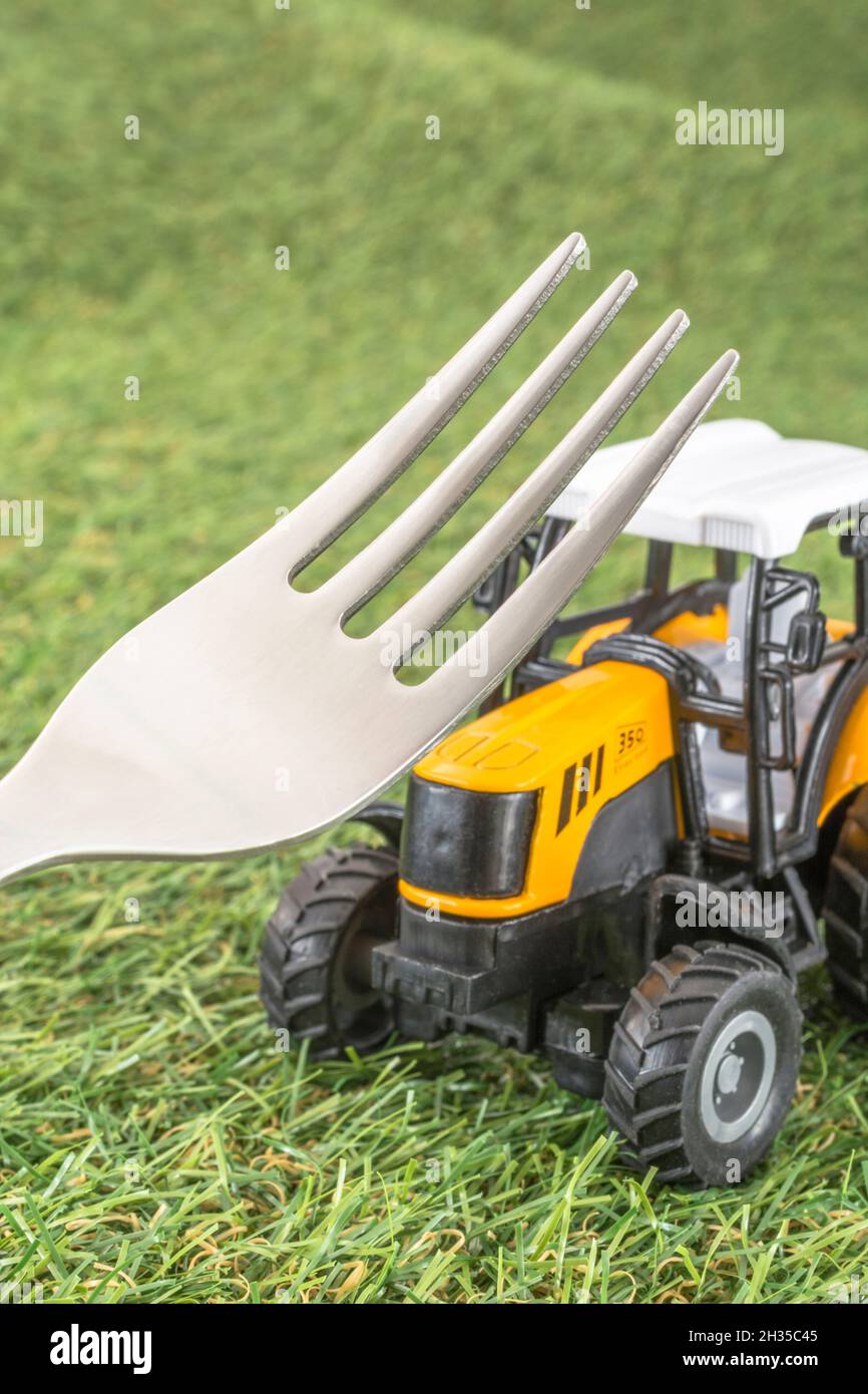 Kleiner Spielzeugschlepper auf faux/fake Gras mit Edelstahlgabelzinken. Für die britische Lebensmittelproduktion: Farm to Fork, Field to Fork / Field to Plate Idiome. Stockfoto