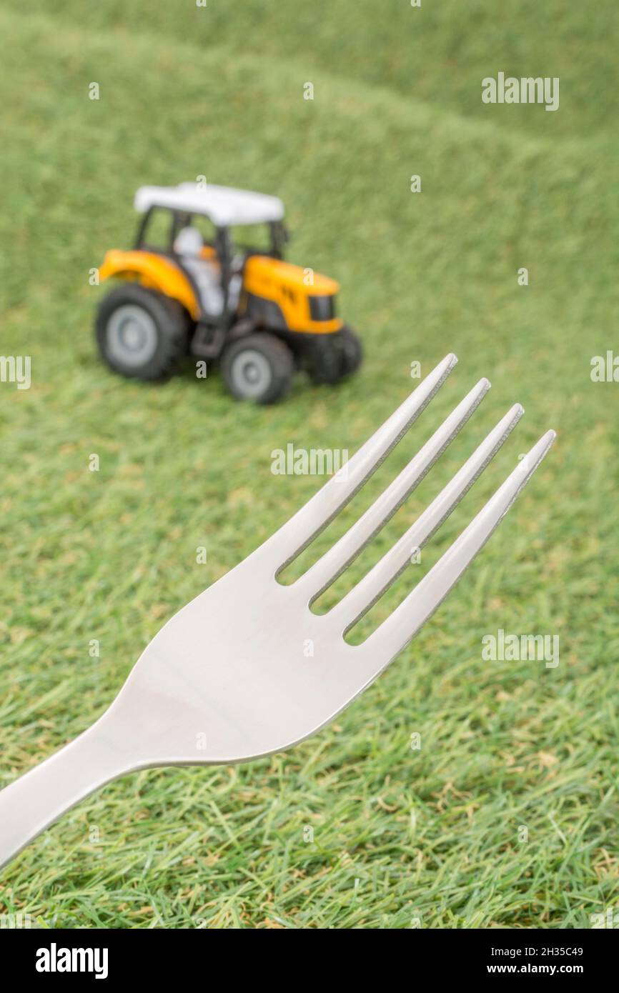 Kleiner Spielzeugschlepper auf faux/fake Gras mit Edelstahlgabelzinken. Für die britische Lebensmittelproduktion: Farm to Fork, Field to Fork / Field to Plate Idiome. Stockfoto