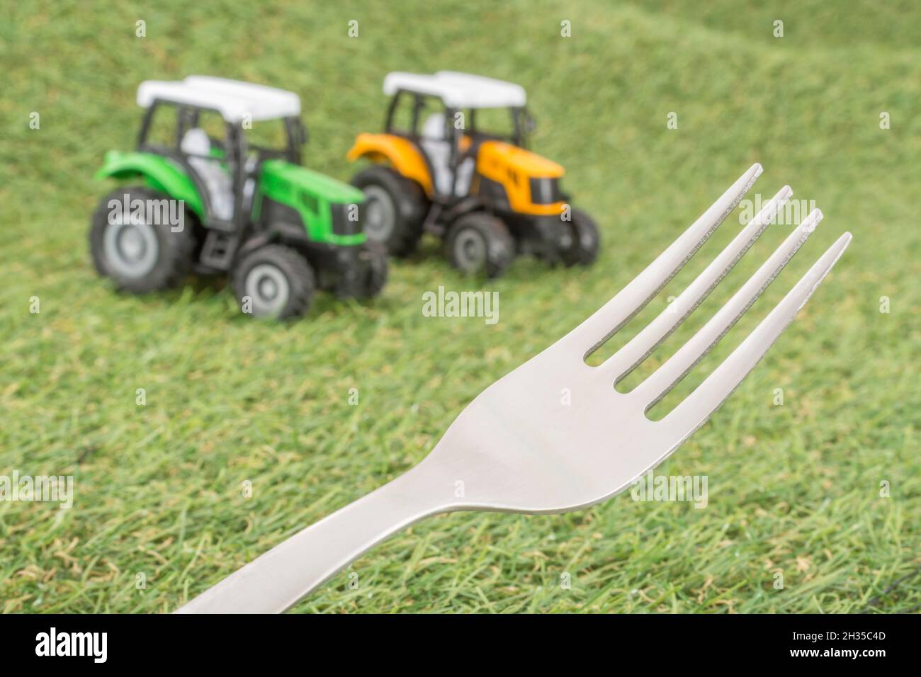 Kleiner Spielzeugschlepper auf faux/fake Gras mit Edelstahlgabelzinken. Für die britische Lebensmittelproduktion: Farm to Fork, Field to Fork / Field to Plate Idiome. Stockfoto