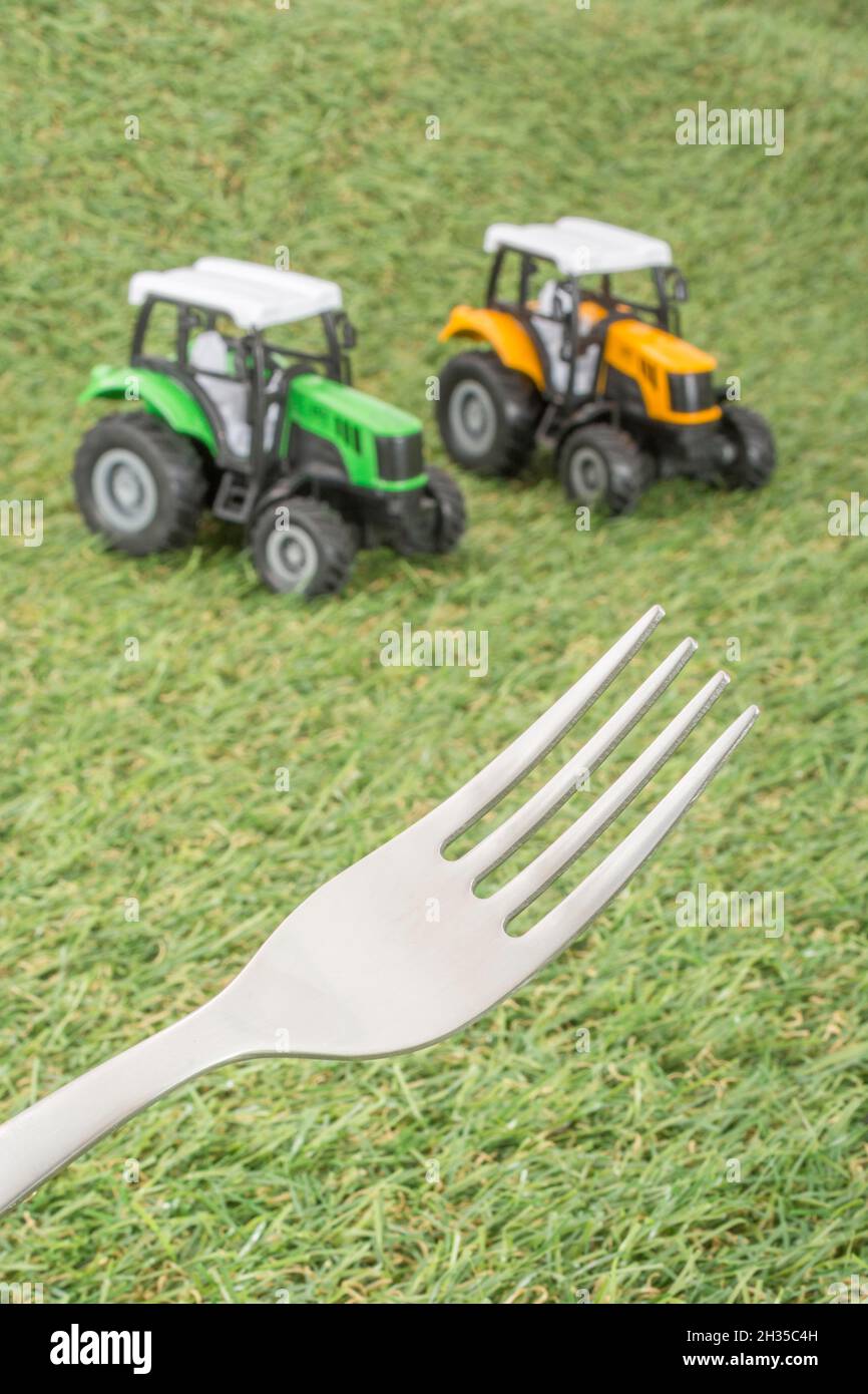 Kleiner Spielzeugschlepper auf faux/fake Gras mit Edelstahlgabelzinken. Für die britische Lebensmittelproduktion: Farm to Fork, Field to Fork / Field to Plate Idiome. Stockfoto