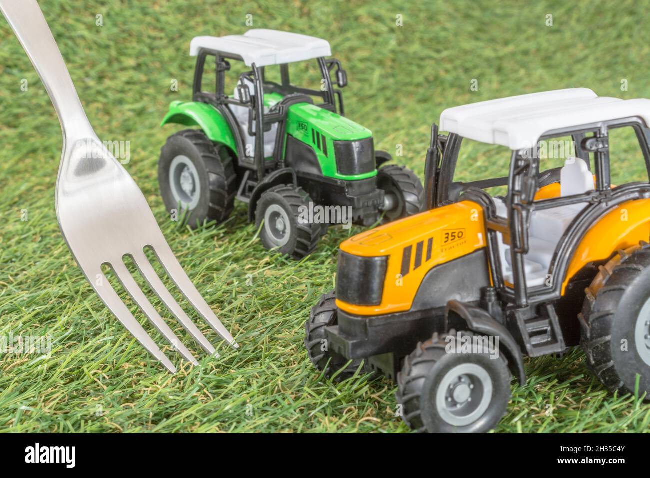 Kleiner Spielzeugschlepper auf faux/fake Gras mit Edelstahlgabelzinken. Für die britische Lebensmittelproduktion: Farm to Fork, Field to Fork / Field to Plate Idiome. Stockfoto