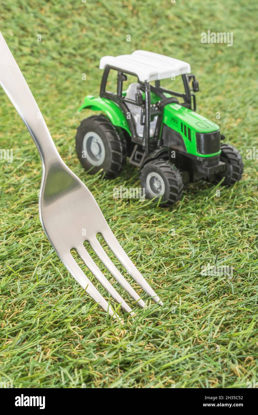 Kleiner Spielzeugschlepper auf faux/fake Gras mit Edelstahlgabelzinken. Für die britische Lebensmittelproduktion: Farm to Fork, Field to Fork / Field to Plate Idiome. Stockfoto
