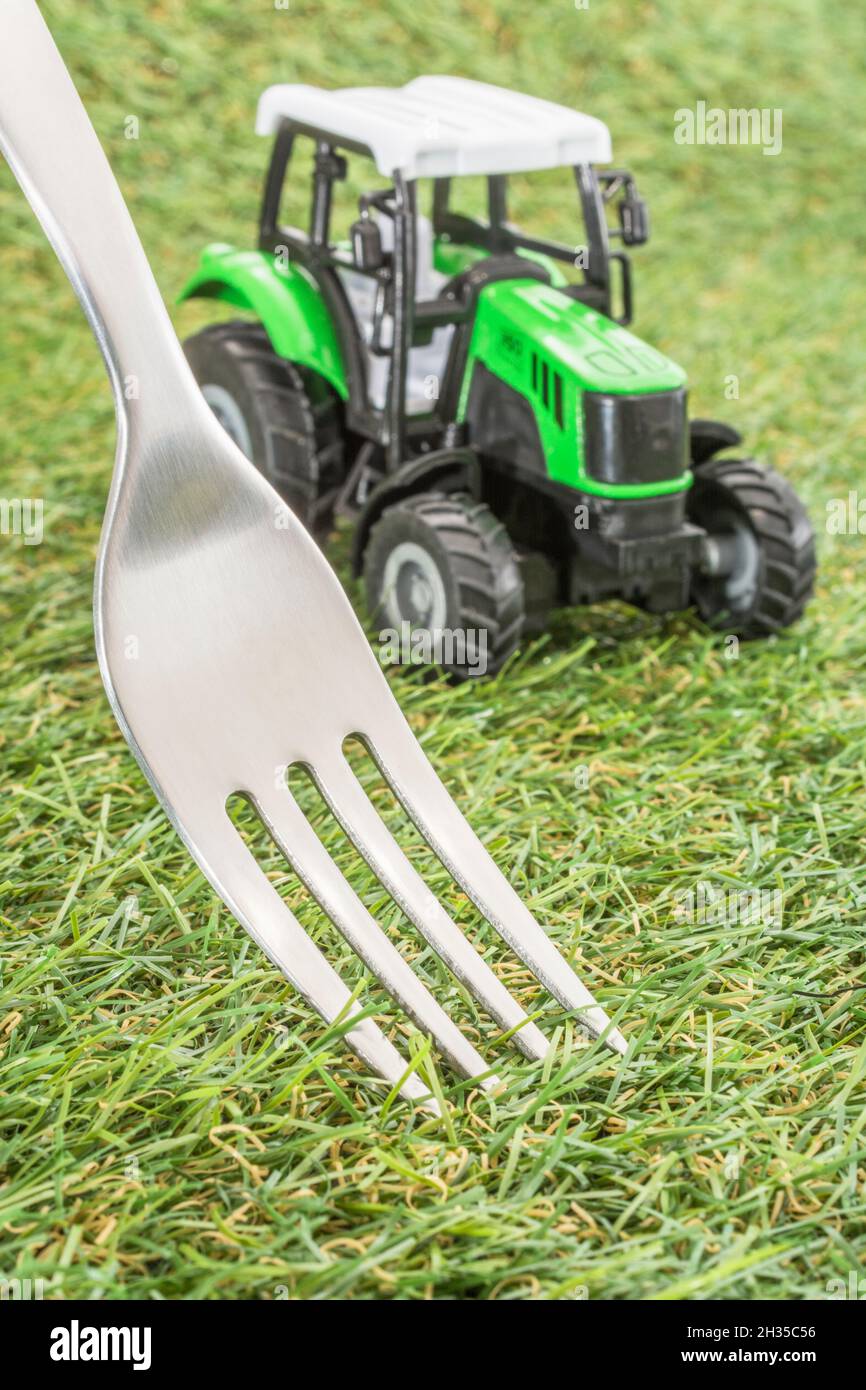 Kleiner Spielzeugschlepper auf faux/fake Gras mit Edelstahlgabelzinken. Für die britische Lebensmittelproduktion: Farm to Fork, Field to Fork / Field to Plate Idiome. Stockfoto