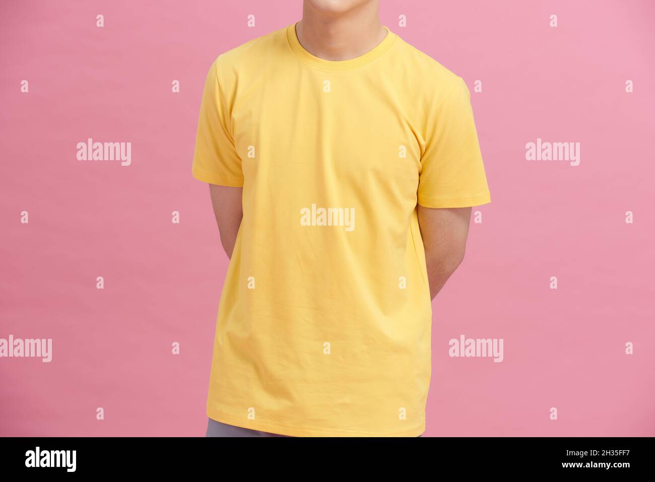 Teilansicht eines Mannes in gelbem T-Shirt, der die Hände hinter dem Rücken hält, isoliert auf rosa Stockfoto