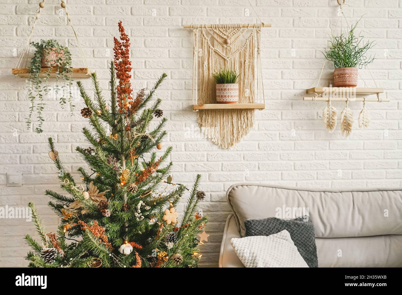 Weihnachten und Neujahr Dekorationen in modernem Wohndesign mit Sofa und Macrame-Paneelen. Boho-Design. Weihnachtsbaum geschmückt mit dr Stockfoto