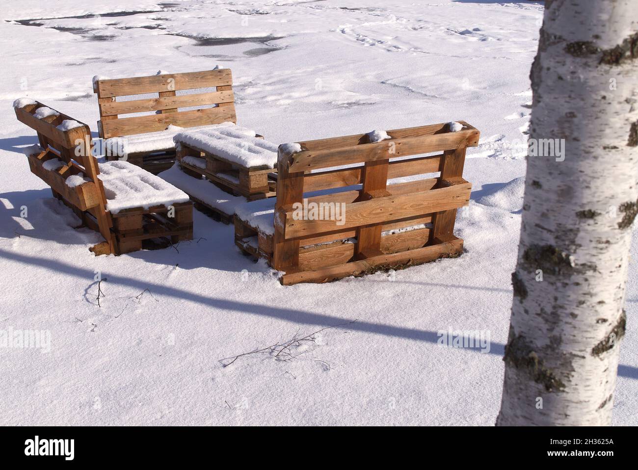 Verschneite Gartenmöbel aus Holzpaletten im Winter in der Nähe Birken Stockfoto