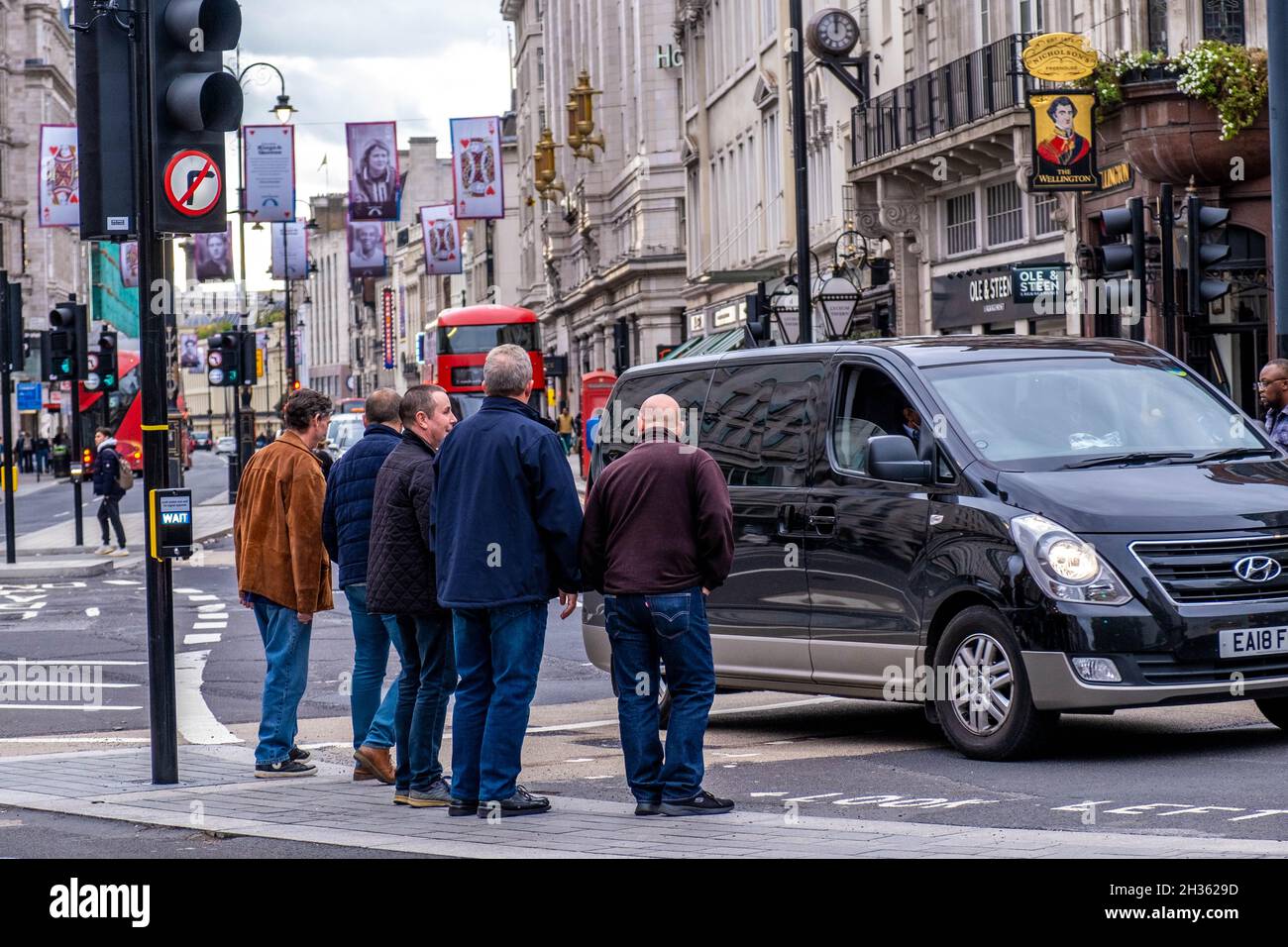 Eine Gruppe von Männern mittleren Alters, die an der Ampel in der City of Westminster in London, Großbritannien, stehen, um die Straße zu überqueren Stockfoto