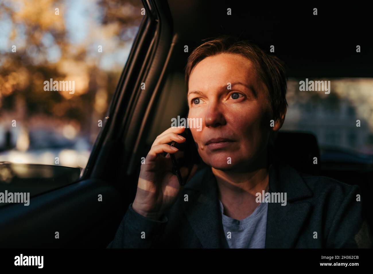 Seriöse Geschäftsfrau, die auf dem Rücksitz des Autos auf dem Mobiltelefon spricht, selektiver Fokus Stockfoto