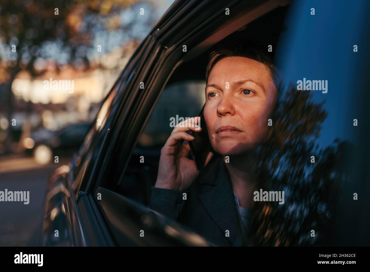 Seriöse Geschäftsfrau, die auf dem Rücksitz des Autos auf dem Mobiltelefon spricht, selektiver Fokus Stockfoto