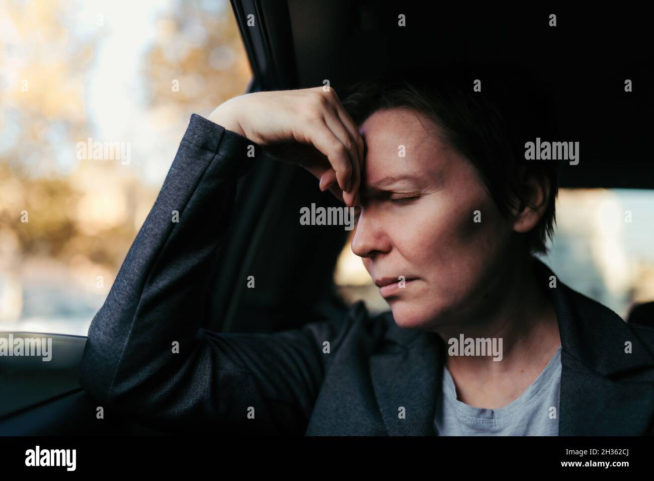 Geschäftsfrau mit starken Kopfschmerzen, die auf dem Rücksitz eines Autos sitzt, selektiver Fokus Stockfoto