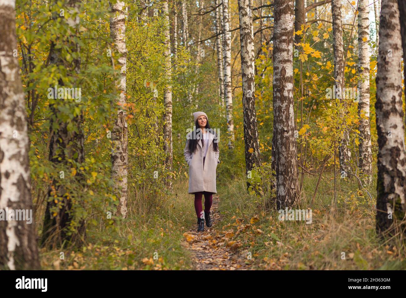 Porträt einer fröhlichen jungen Frau, die im Herbstpark genießt. Schöne Brünette Mädchen im Herbst grauen Mantel und gestrickten Hut. Entspannen Sie sich in der Natur. Stockfoto