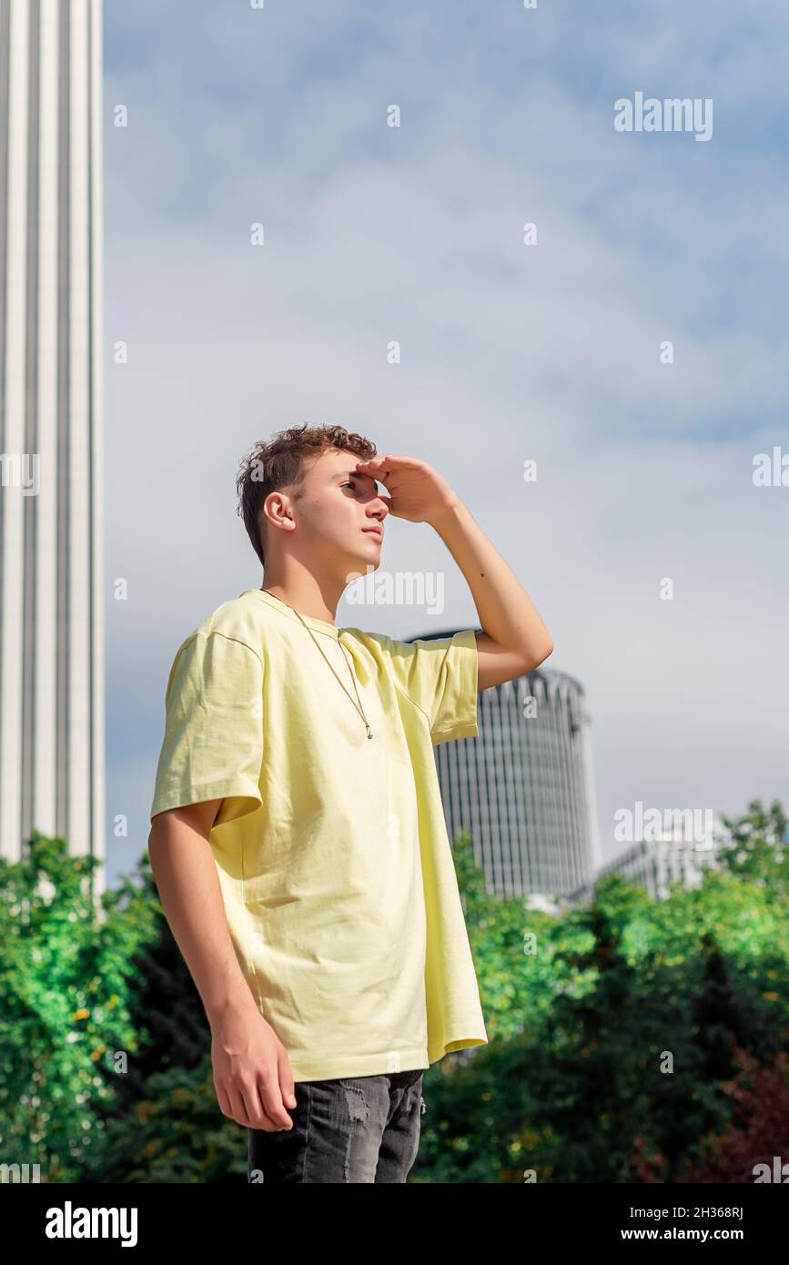 Junger Mann im gelben T-Shirt, der mit der Hand auf der Stirn den Horizont anschaut Stockfoto