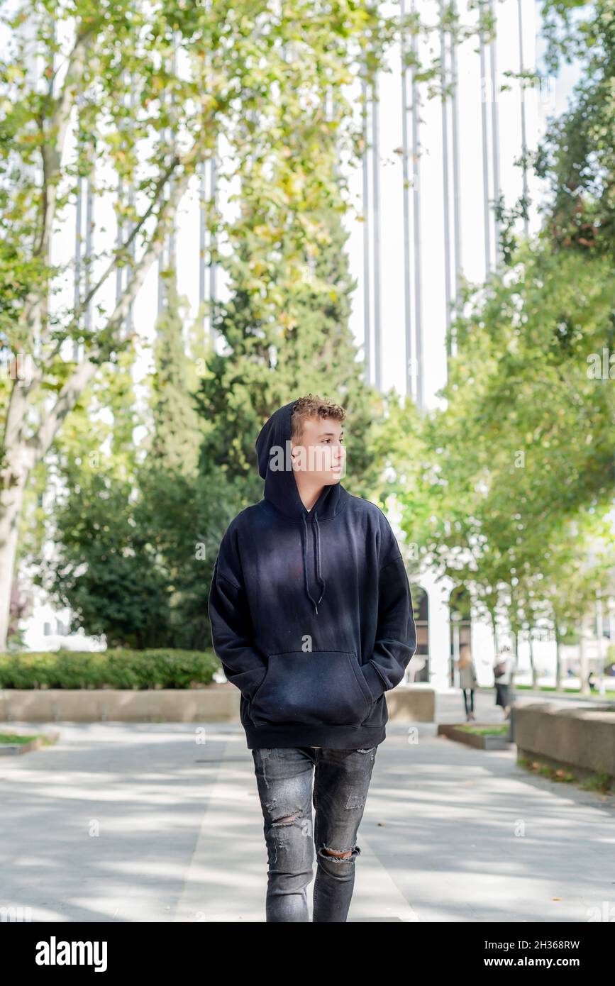 Ein junger Mann, der die Straße entlang geht, trägt ein schwarzes Sweatshirt und einen Hoodie Stockfoto