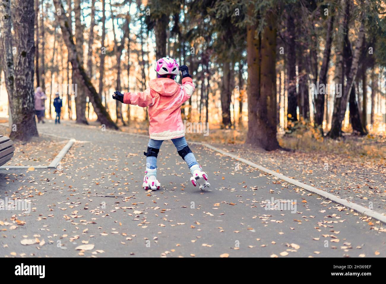 Kid girl in einem rosa Helm reitet in einem Herbstpark auf vier Rädern Rollen. Herbst Outdoor-Aktivitäten Stockfoto