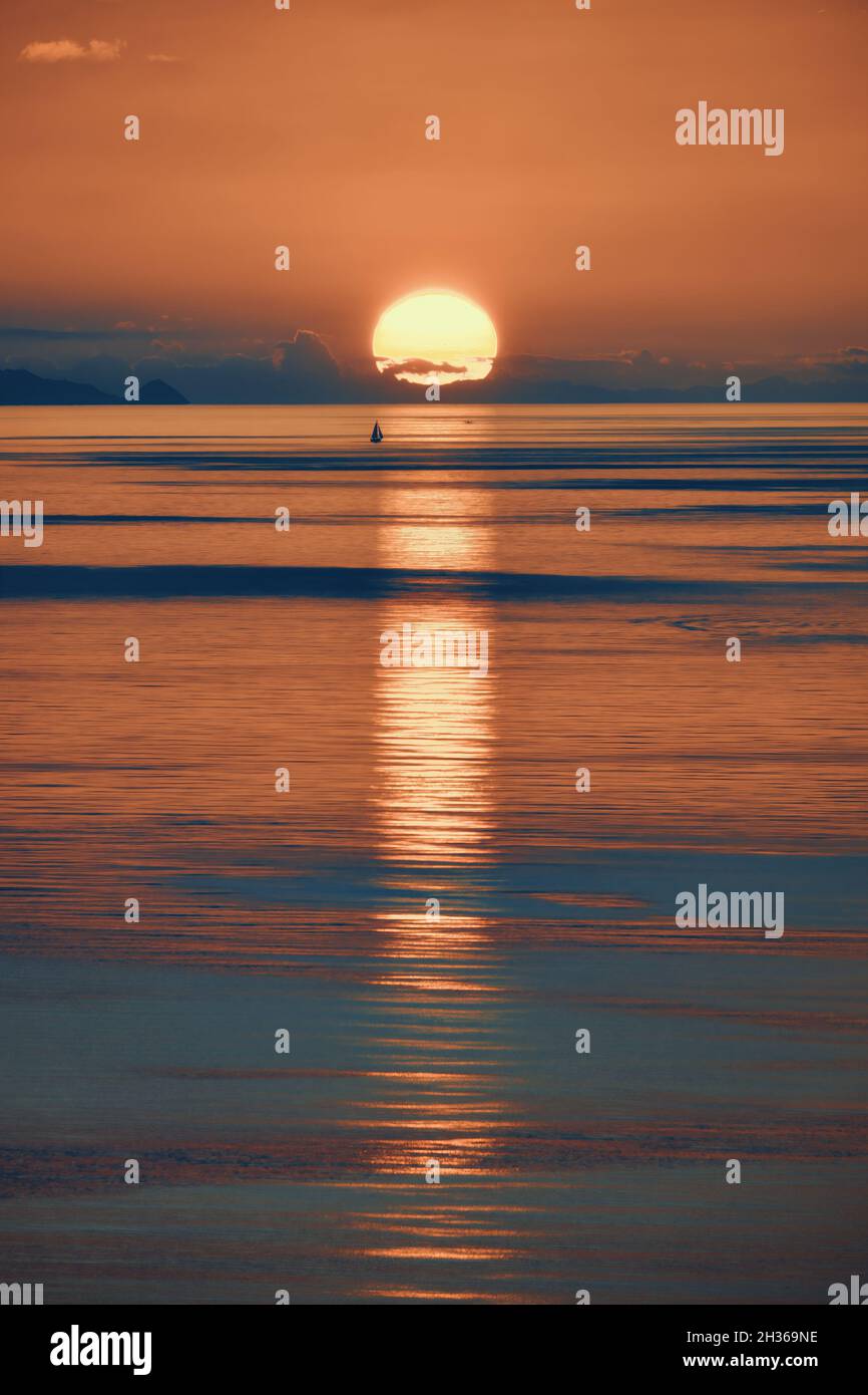 Abgelegenes Segelboot am Horizont mit den Reflexionen im Wasser des Sonnenuntergangs von Capo Milazzo in Sizilien, Italien Stockfoto