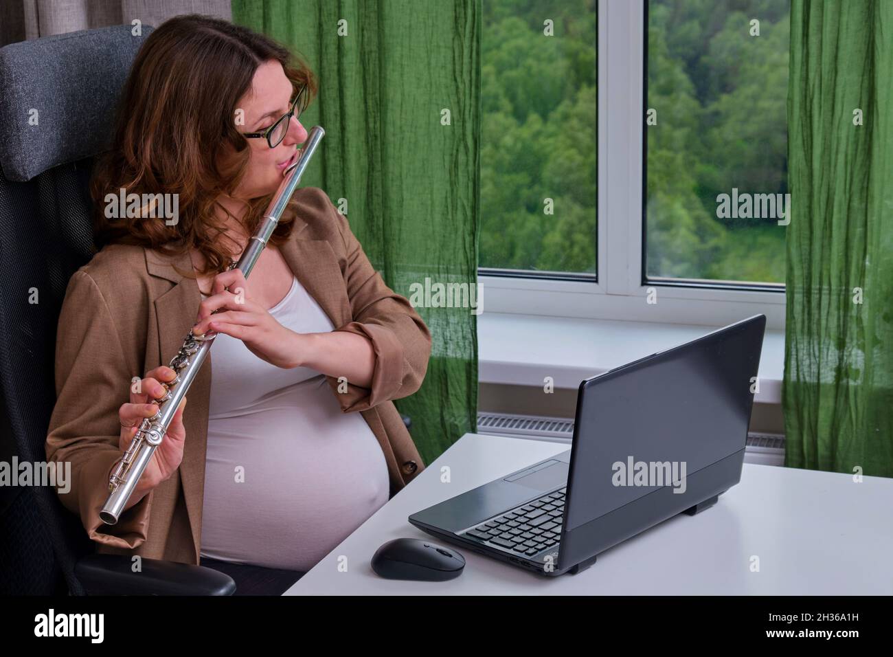 Schwanger Frau mit Laptop im Heimbüro lernen, Musikinstrument zu spielen Stockfoto