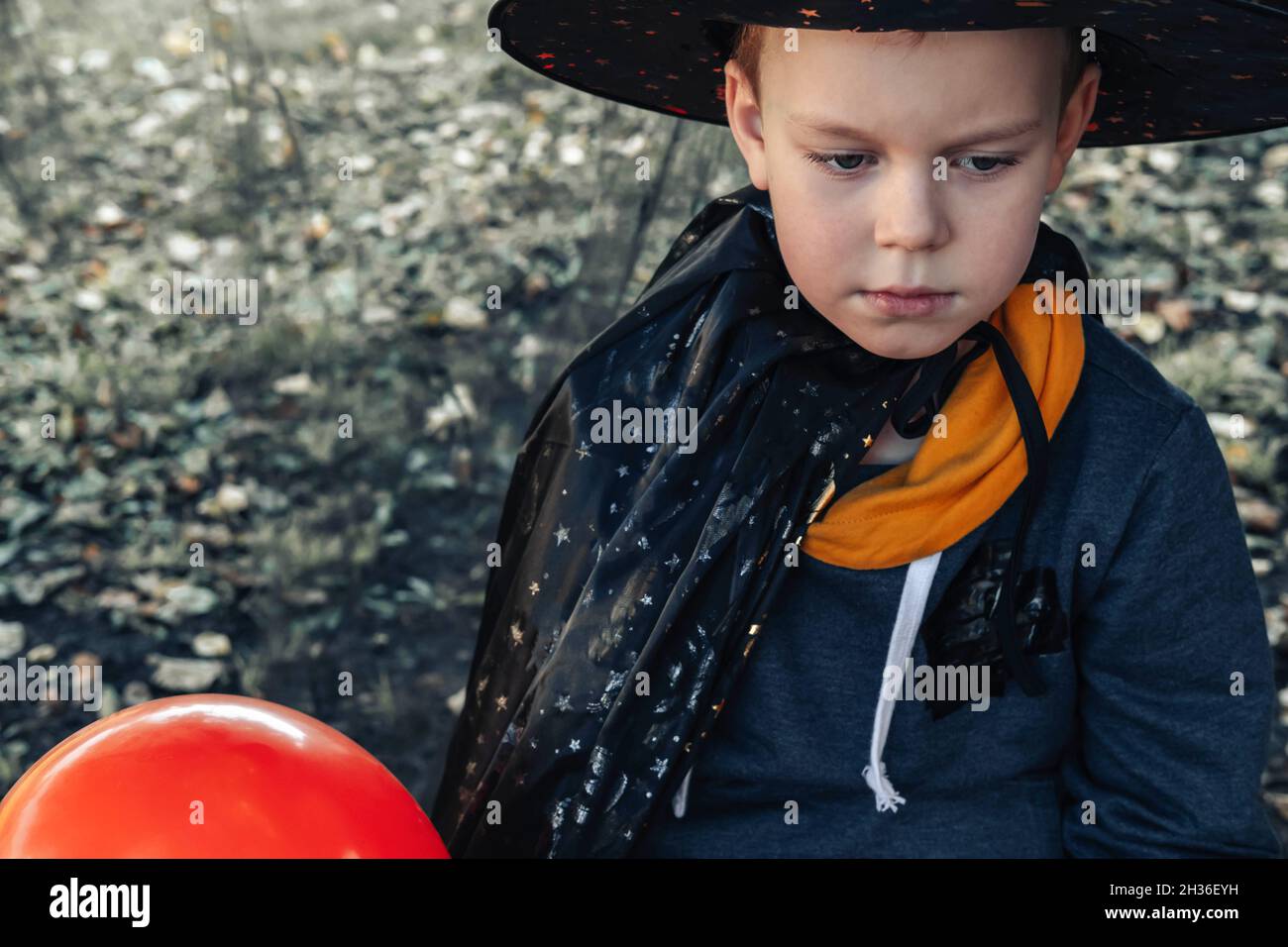 Halloween Kinder. Niedlicher kleiner Junge traurig an Halloween, Kind im Hexenhut mit orangefarbenem Jack O Laterne Ballon. Stockfoto