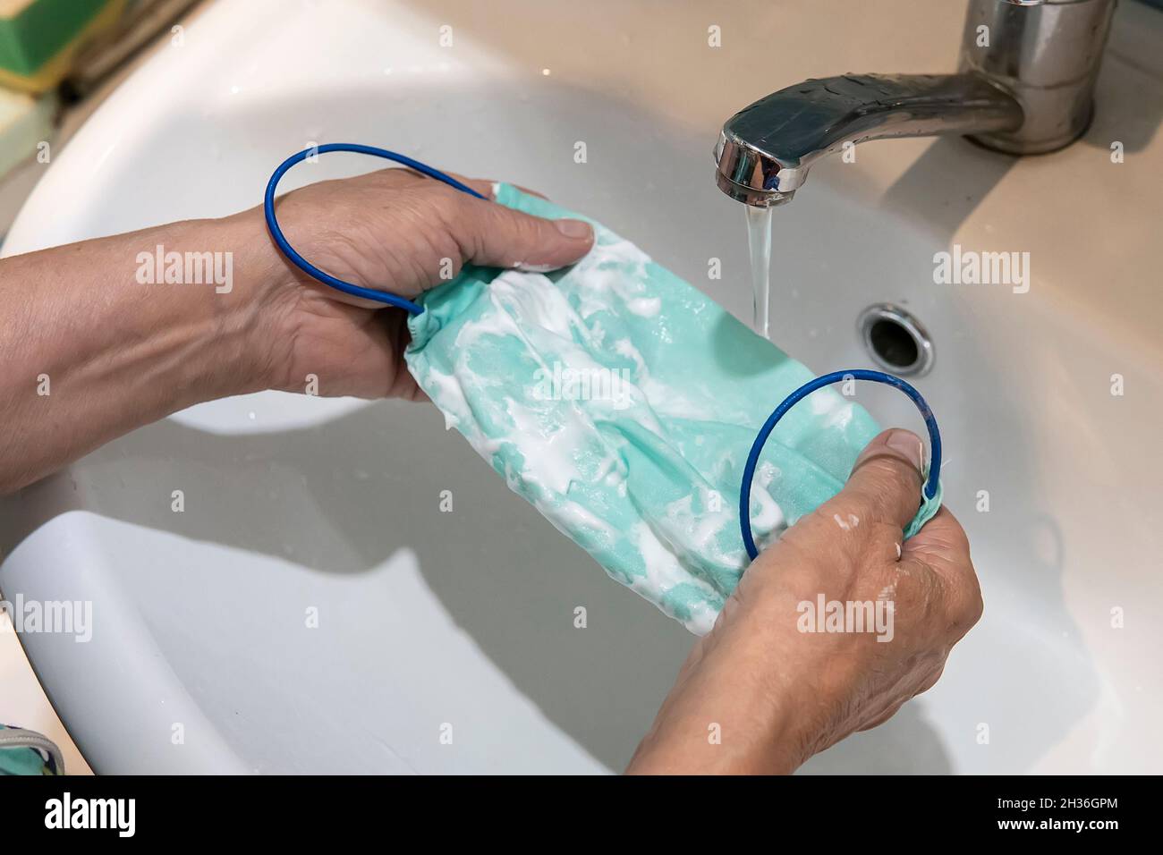 Waschen einer Maske mit in Wasser gelöstem Reinigungsmittel. Das Waschen der Masken desinfiziert und spart Geld, um wieder verwendet zu werden. Stockfoto