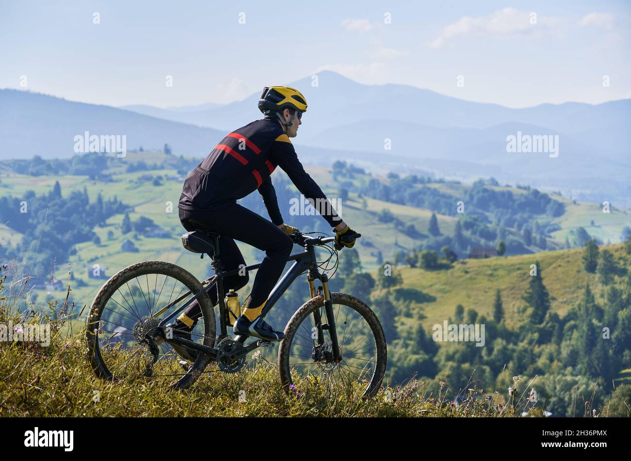 Mann, der am frühen nebligen Morgen mit dem Fahrrad in den Bergen fährt und bergab fährt. Gipfel in Wolken, grüne Hügel im Hintergrund. Seitenansicht. Konzept des aktiven Lebensstils Stockfoto