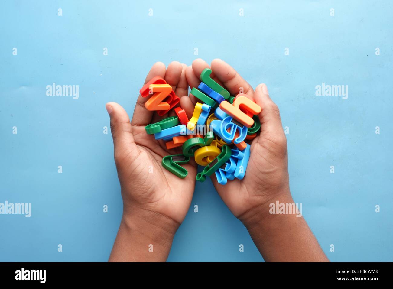 Bunte Plastikbriefe auf Kinderhand auf blauem Hintergrund Stockfoto